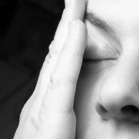 Close-up of a person's face with their hand covering part of their cheek, showing closed eyes and partially visible nose.