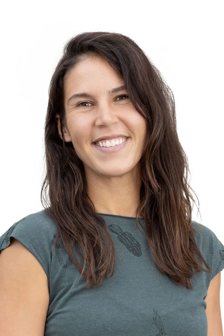 A woman with long, wavy brown hair, smiling, wearing a green T-shirt with a graphic design of a chili pepper.