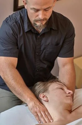 A man providing a massage or chiropractic adjustment to a woman lying face down on a massage table.