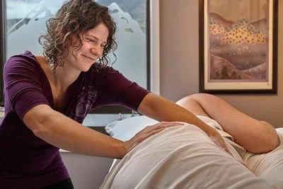 A woman giving a massage to a person lying on a bed or massage table.