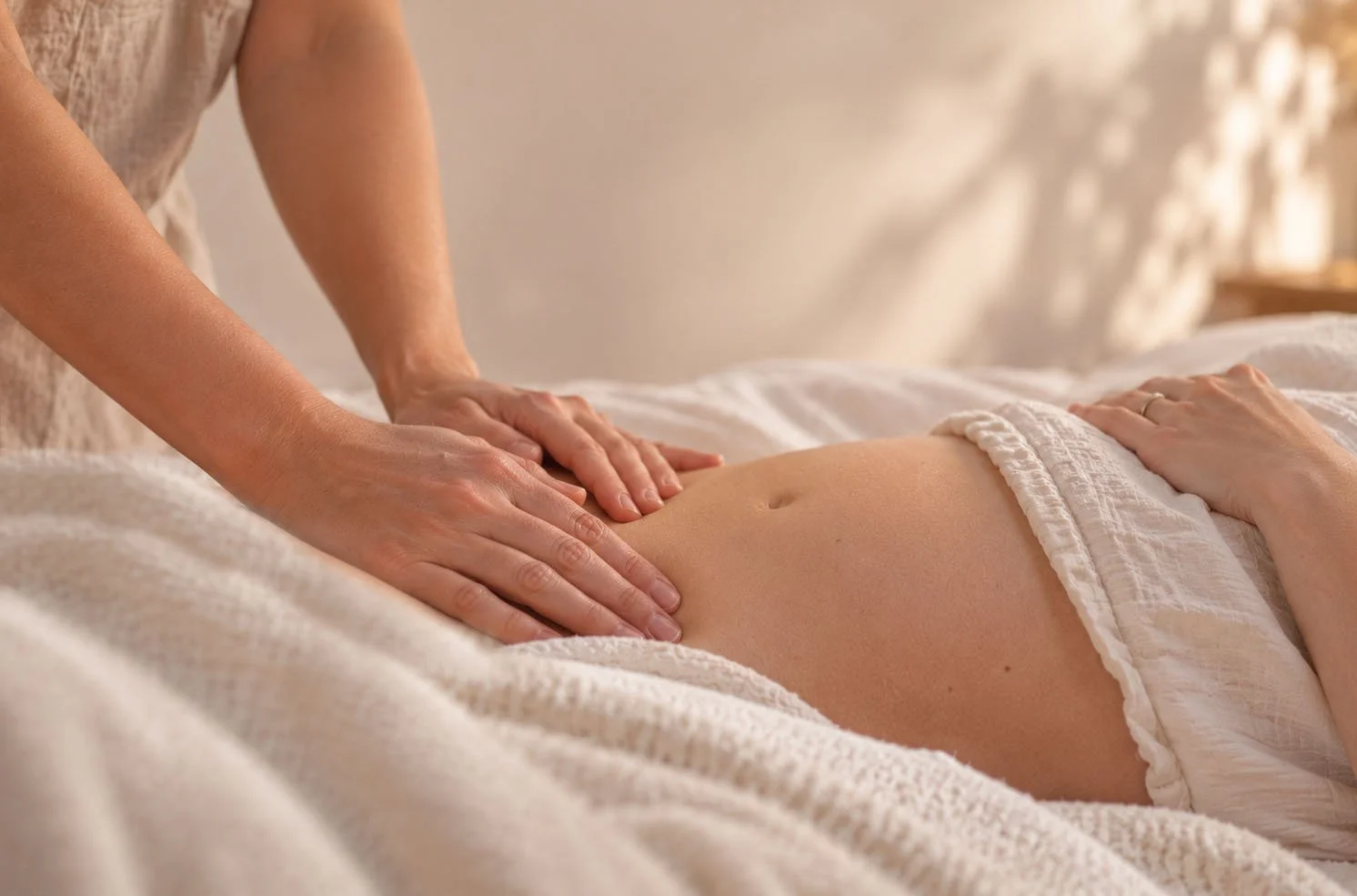 A person giving a massage to another person lying on a bed, focusing on the recipient's abdomen.