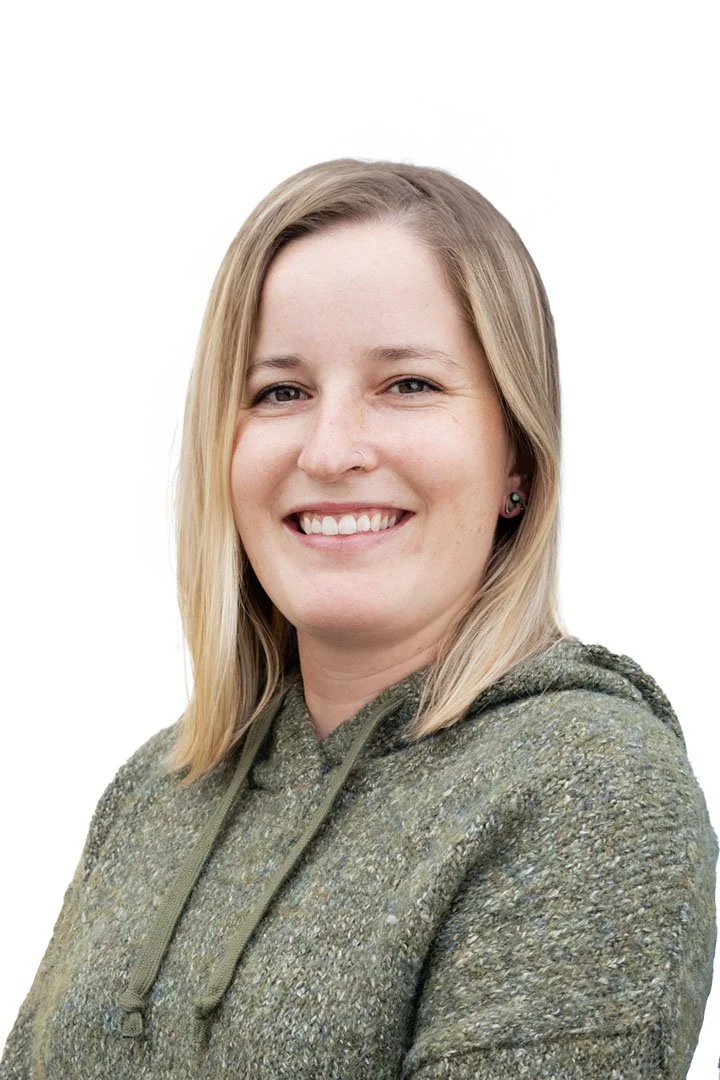A woman with blonde hair, smiling, wearing a green hoodie against a white background.