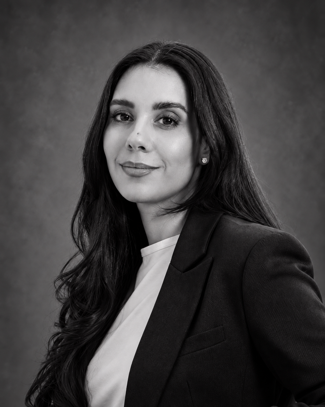 Black and white portrait of a woman with long dark hair, wearing a blazer and a white top, smiling slightly against a plain background.