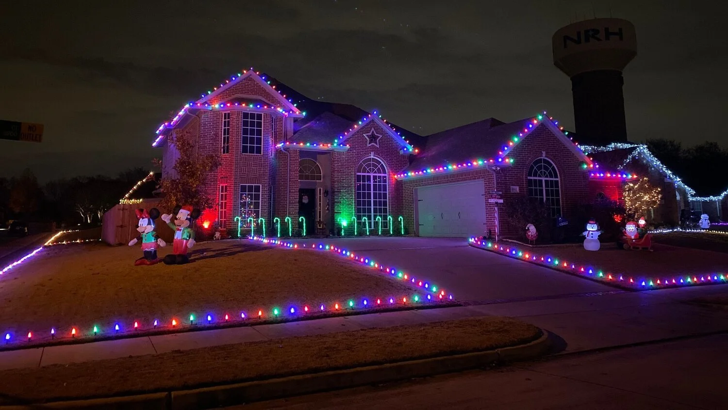 A house decorated with colorful Christmas lights and inflatable holiday figures like snowmen and reindeer during the night.