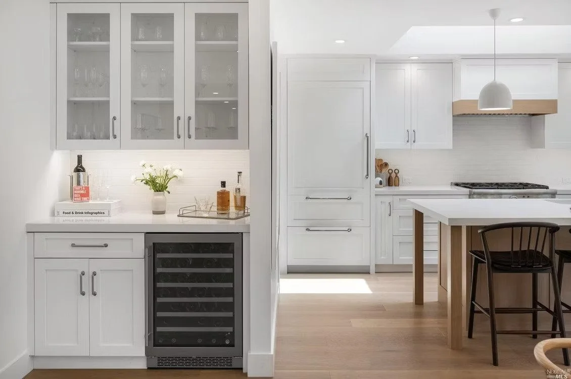 Modern white kitchen with glass-front cabinets, wine fridge, and wooden accents.
