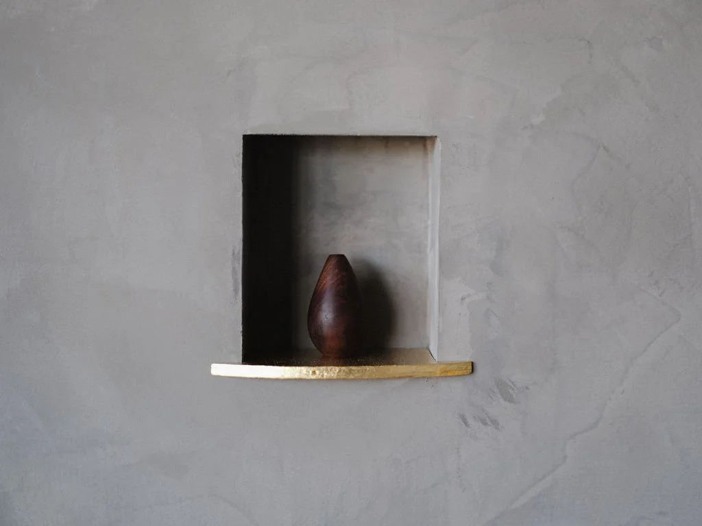 A wooden vase placed on a small ledge within a recessed wall niche, in a minimalist setting.