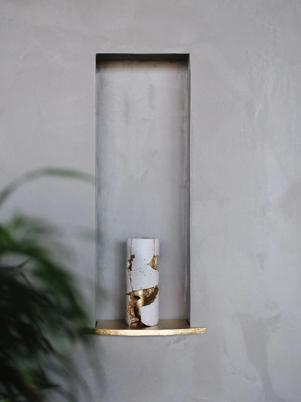 Decorative wall alcove with a small sculpture of a broken white and gold abstract figure on a hidden shelf.