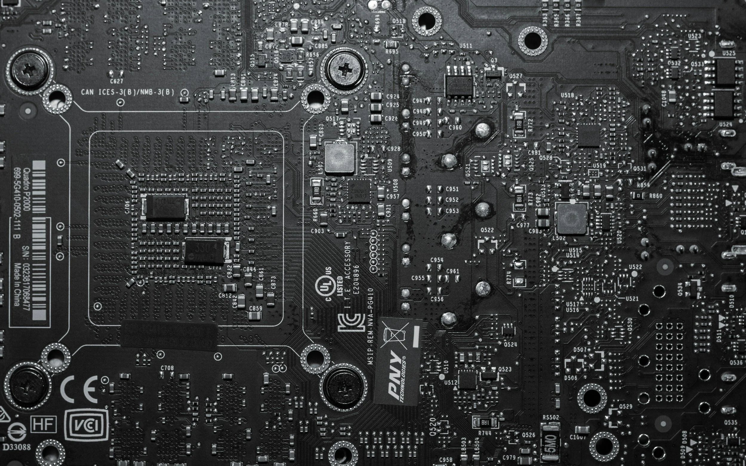 Close-up view of a computer motherboard showing various electronic components, circuits, and labels in black and white.