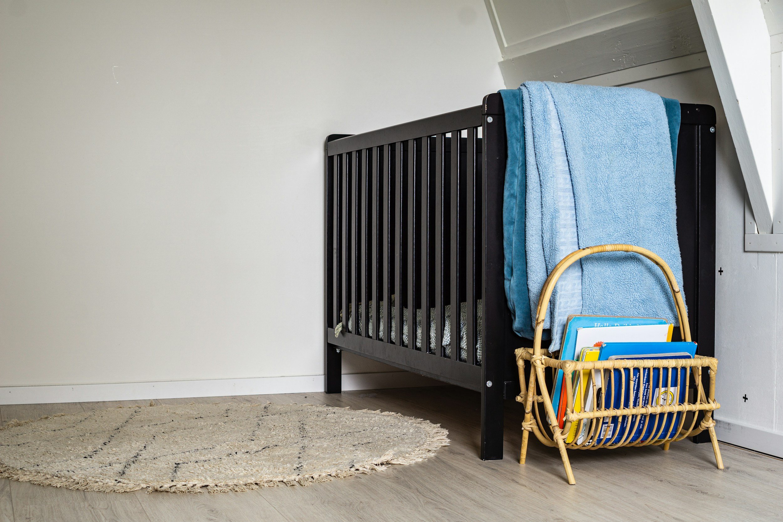 Baby cot in a calm nursery with children's books, soft furnishings and a play area.