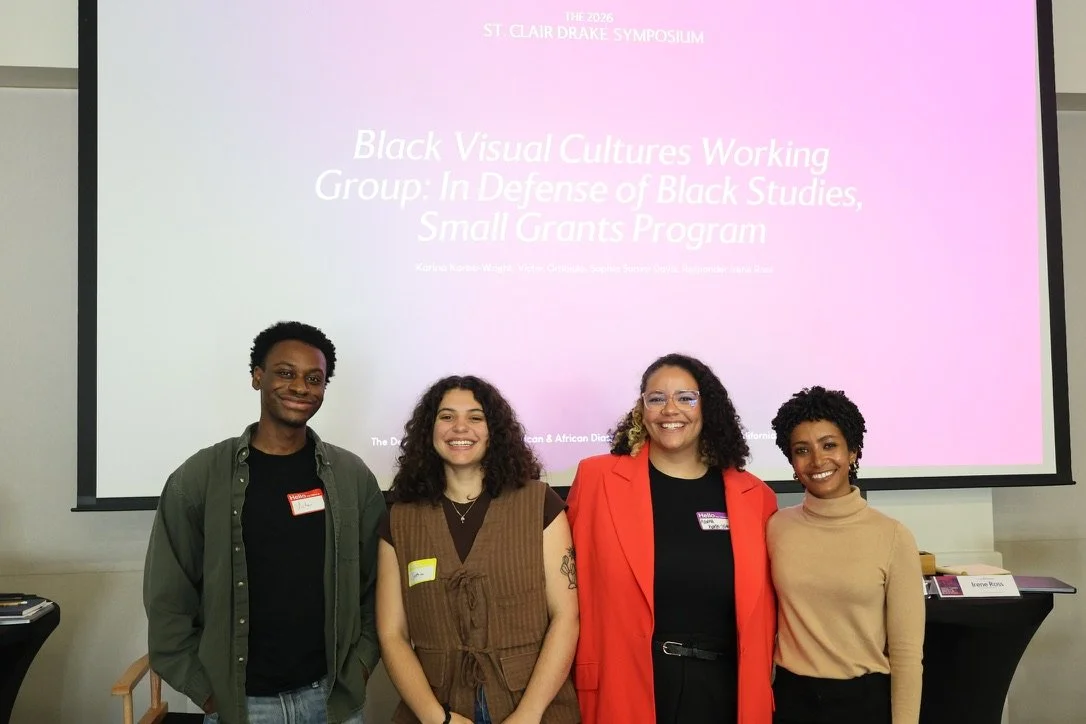 Four people standing in front of a presentation slide that reads 'Black Visual Cultures Working Group: In Defense of Black Studies, Small Grants Program' at the 2026 St. Clair Drake Symposium.