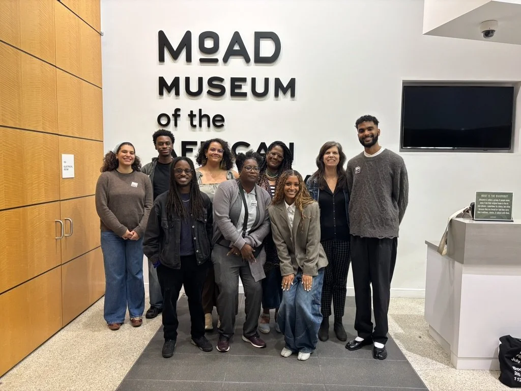 Group of nine people standing in front of a sign that reads "MOAD" inside a building.