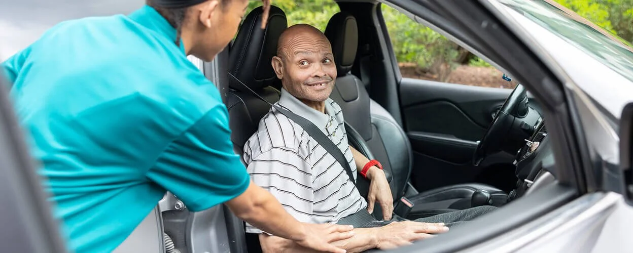 A healthcare worker helping an elderly man get into a car for transportation assistance.