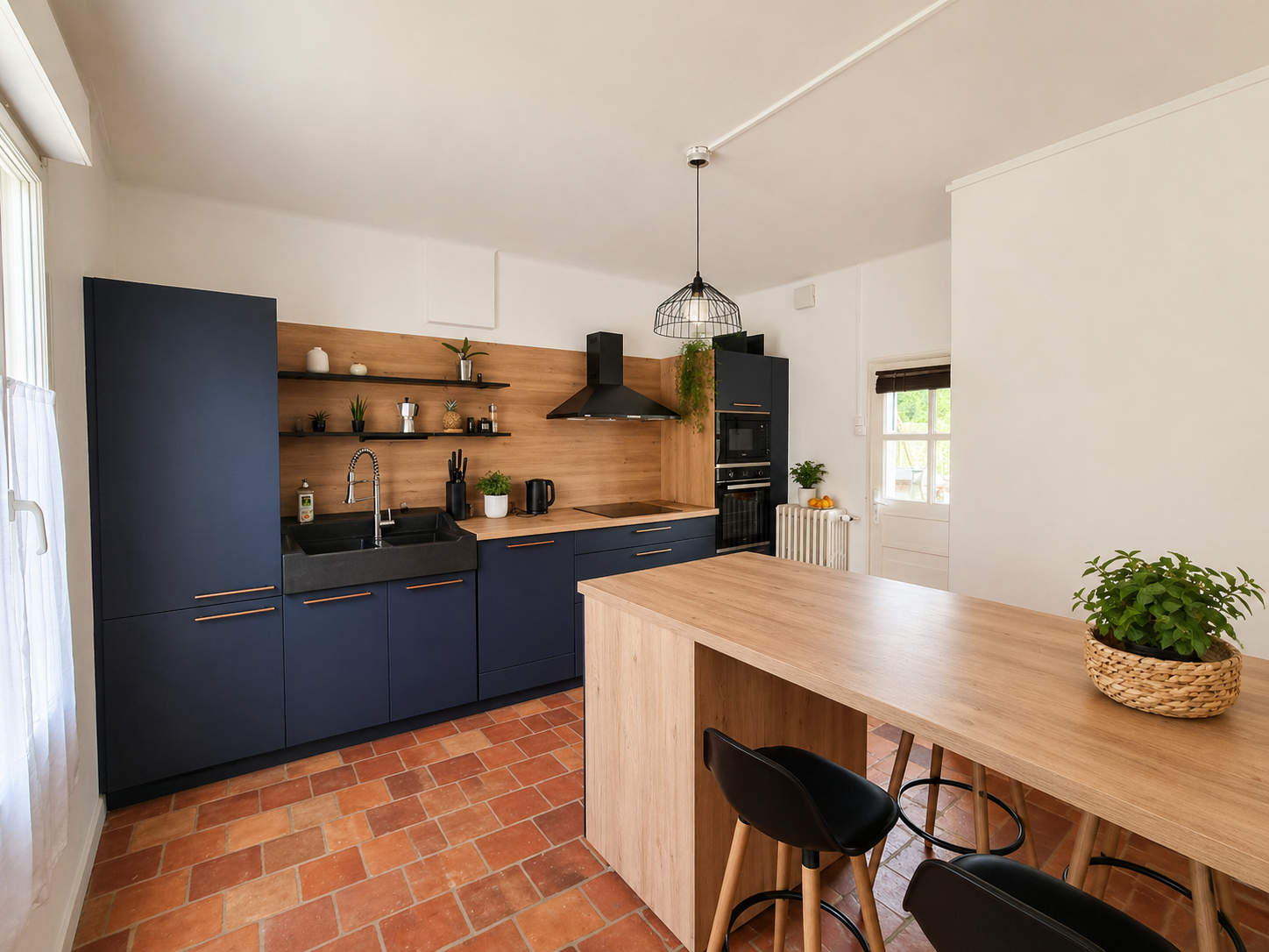 Cuisine moderne avec des meubles bleu foncé, plancher en carreaux de terre cuite, plan de travail en bois clair, étagères avec décorations, plant en pot, et un éclairage suspendu au plafond.