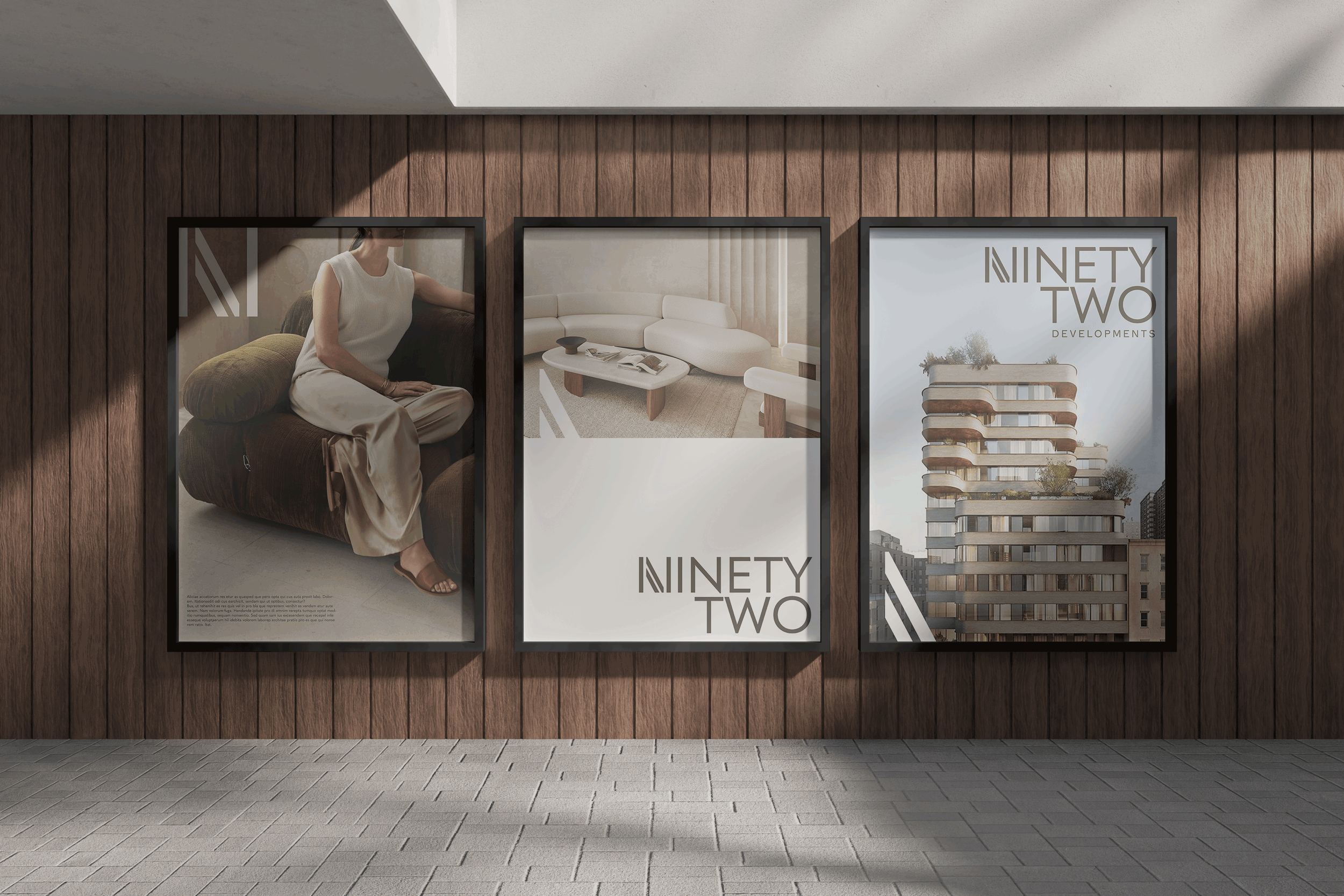 Three framed Ninety Two Developments posters on a wood-paneled wall, featuring a seated woman, a modern living room, and a contemporary apartment building.