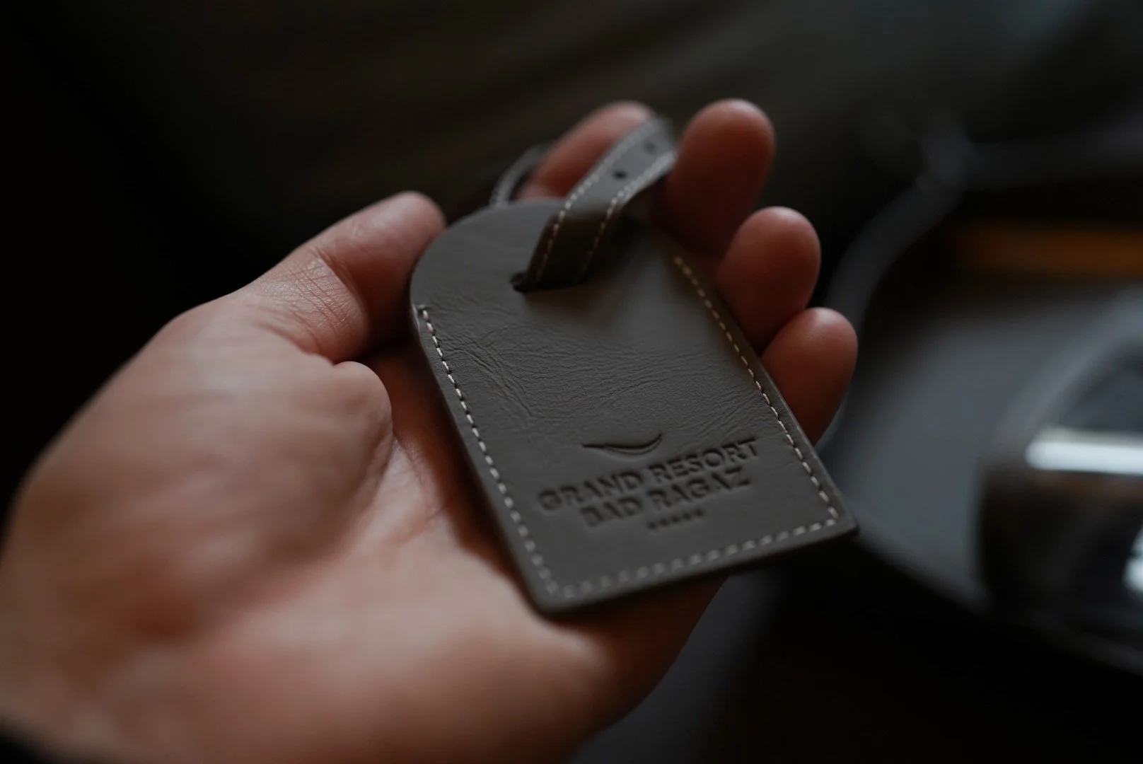 Hand hält einen schwarzen Leder-Schlüsselanhänger mit geprägtem „Grand Resort and Spa“-Logo.