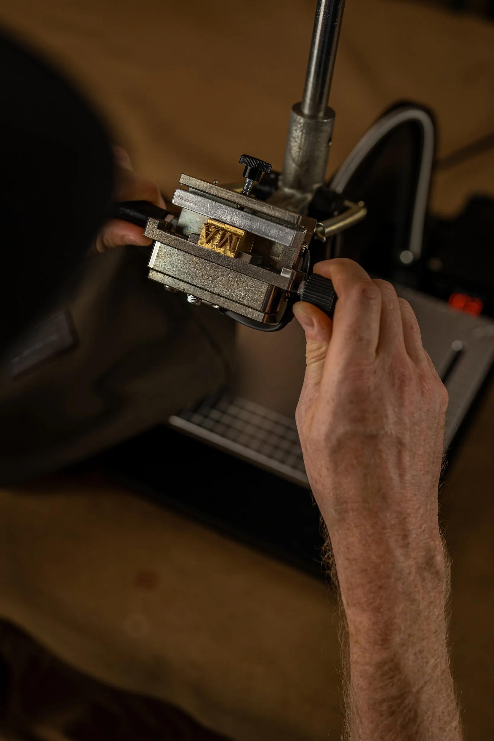 Nahaufnahme eines Gitarrenbauers, der den Hals eines Instruments in einer Metallvorrichtung bearbeitet.