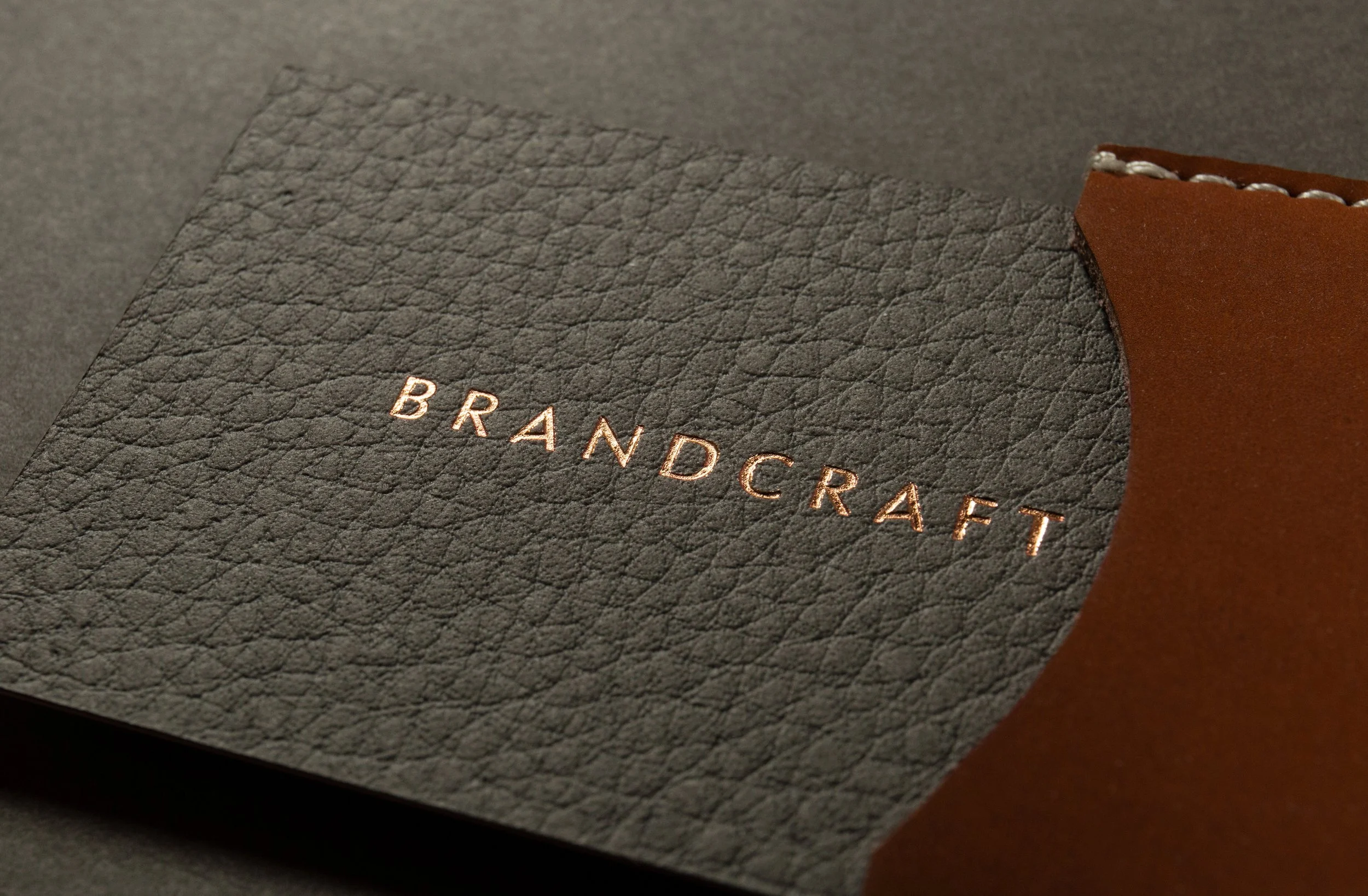 Nahaufnahme eines schwarzen Lederstücks mit Goldschrift, daneben braunes Leder, das genäht ist.