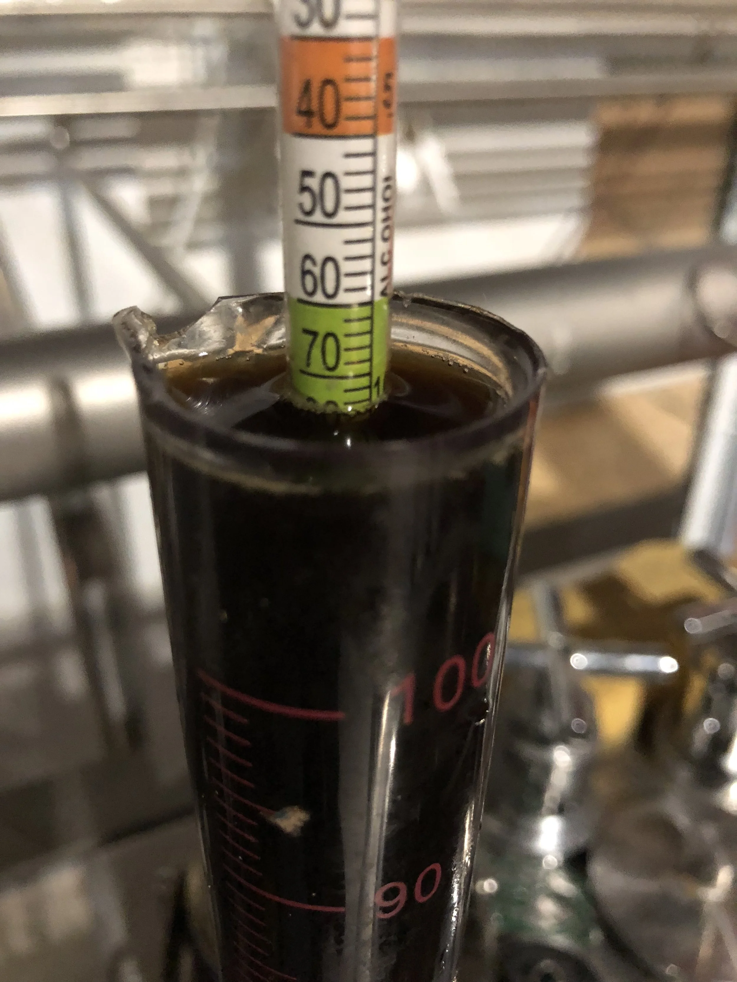 Een glas met donkere koffie en een thermometer die de temperatuur aangeeft, ongeveer 65 graden Celsius.