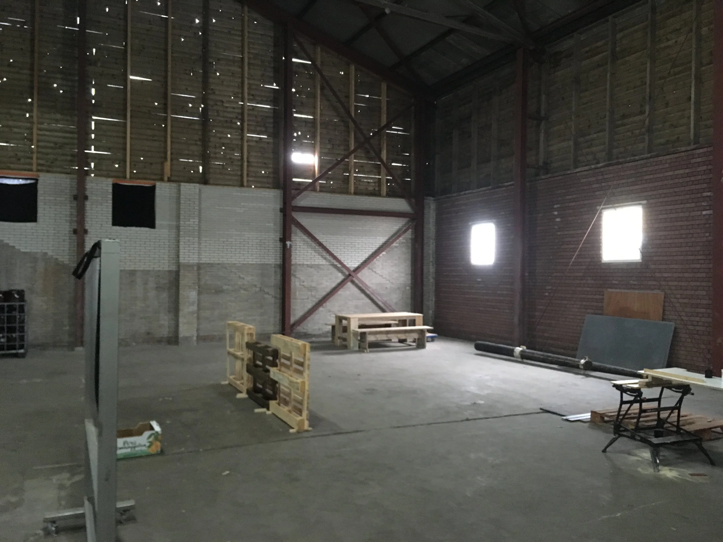 Binnenkant van een bouwplaats of opslagruimte met houten pallets, ramen en metalen steunbalken.