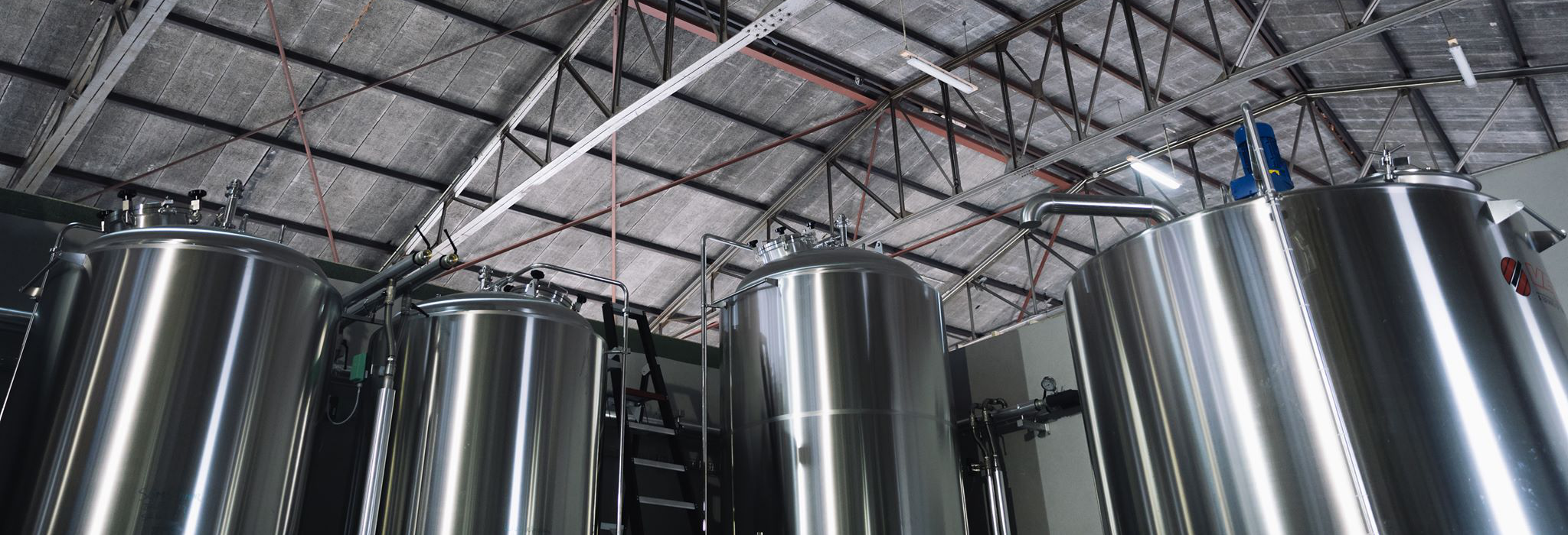 Drie grote roestvrijstalen tanks in een industriële omgeving, met een hoog plafond en metalen ondersteuningen.