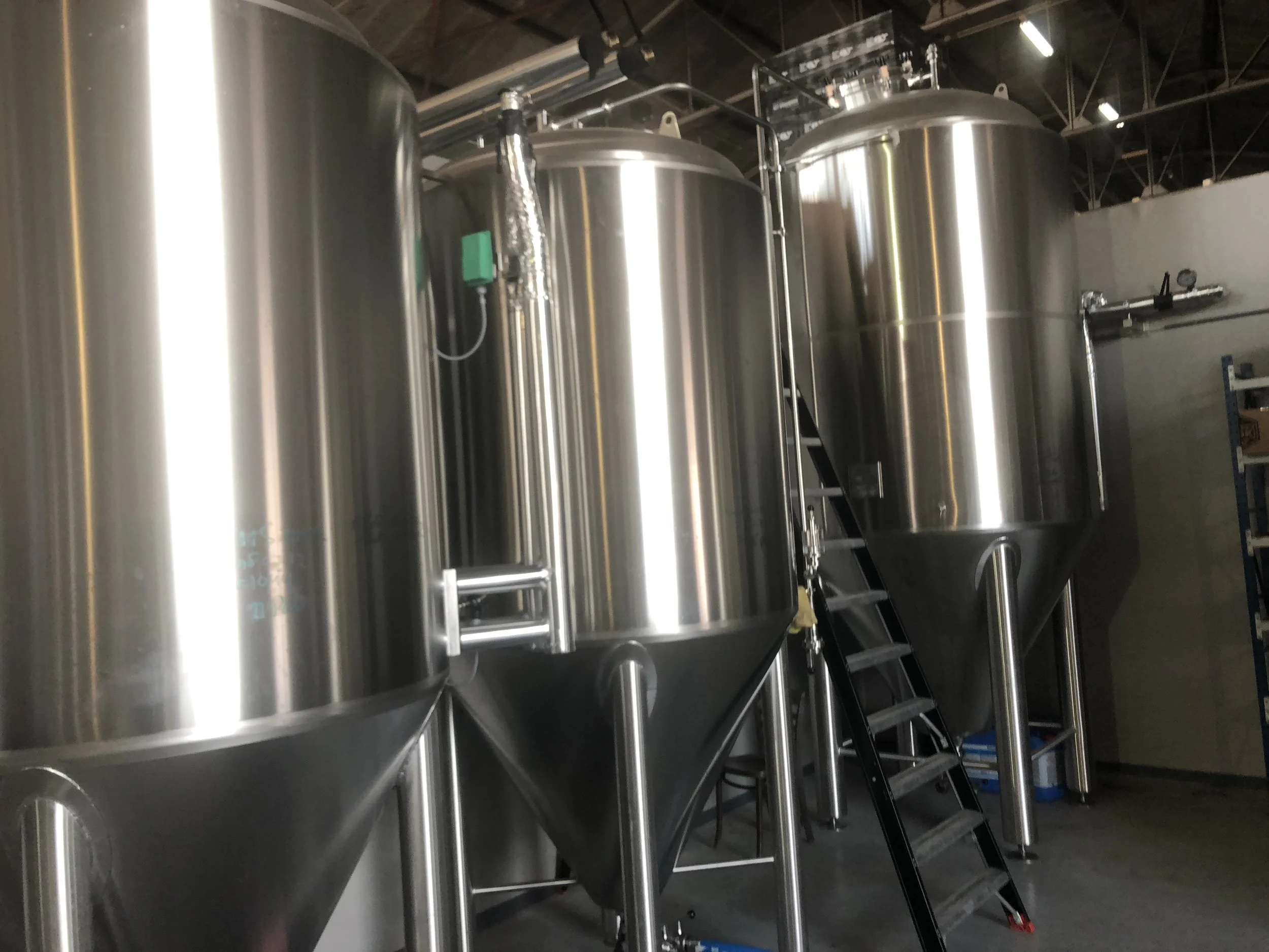 RVS tanks in een industriële setting, mogelijk in een brouwerij of kaasfabriek, met een ladder en meetinstrumenten zichtbaar.