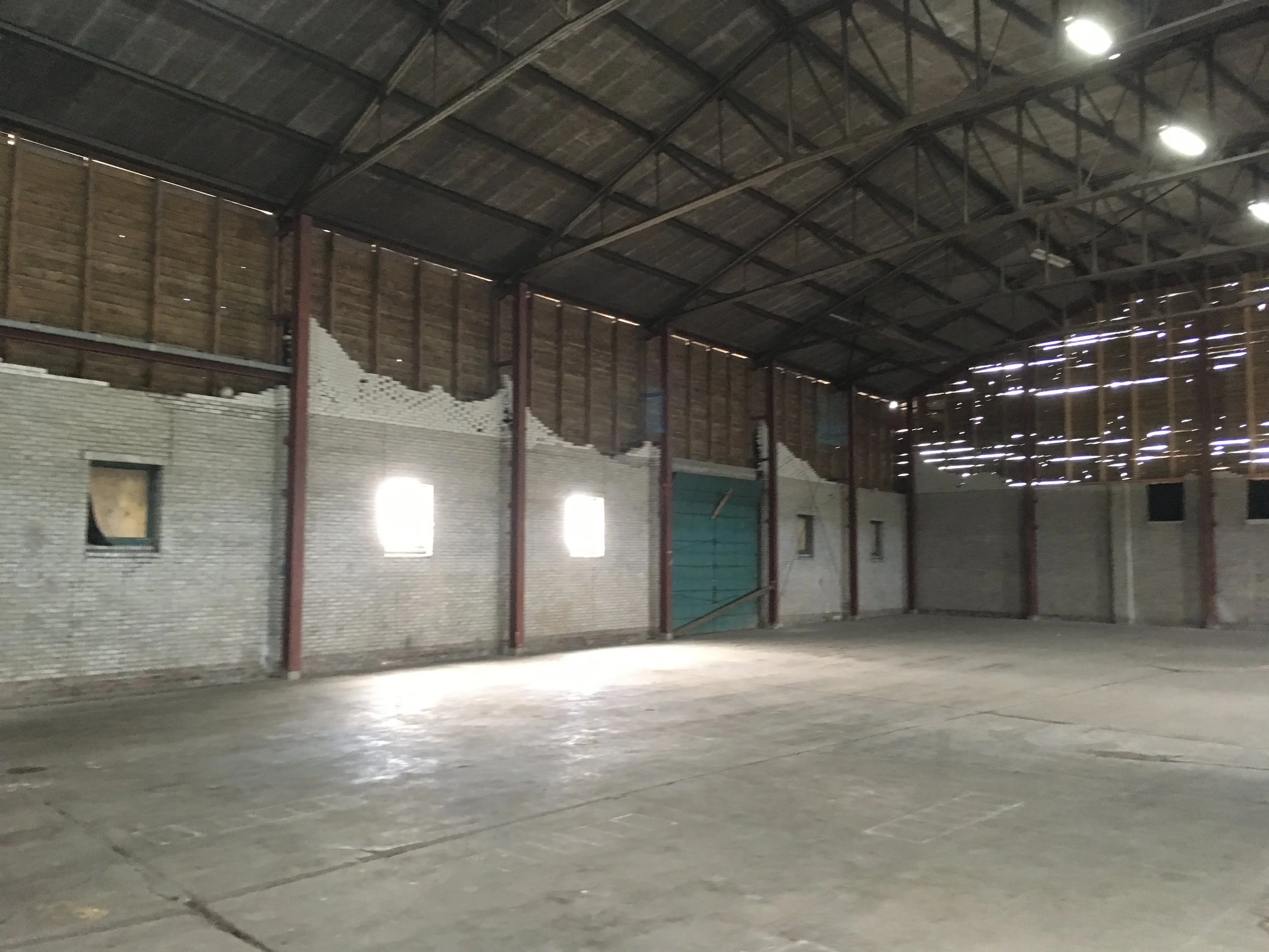 Binnenkant van een leeg industrieel gebouw met een hoge plafond, muurschilderingen en ramen met lichtstralen die naar binnen komen.