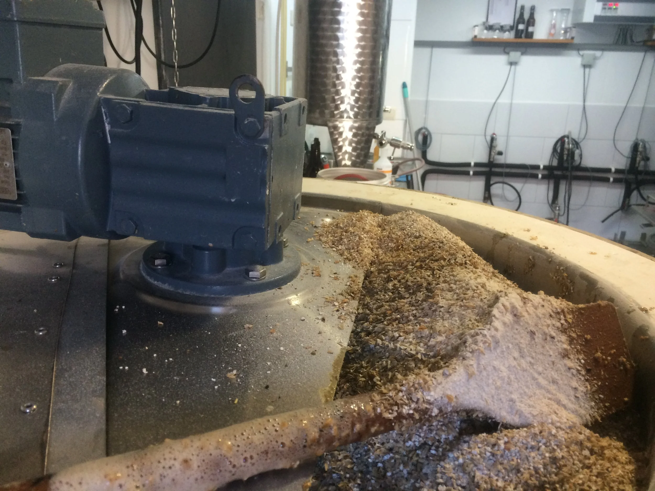 In een brouwerij of bierbrouwerij, met een vat en een met moutstof bedekte oppervlakte, zichtbare apparatuur en leidingen in de achtergrond