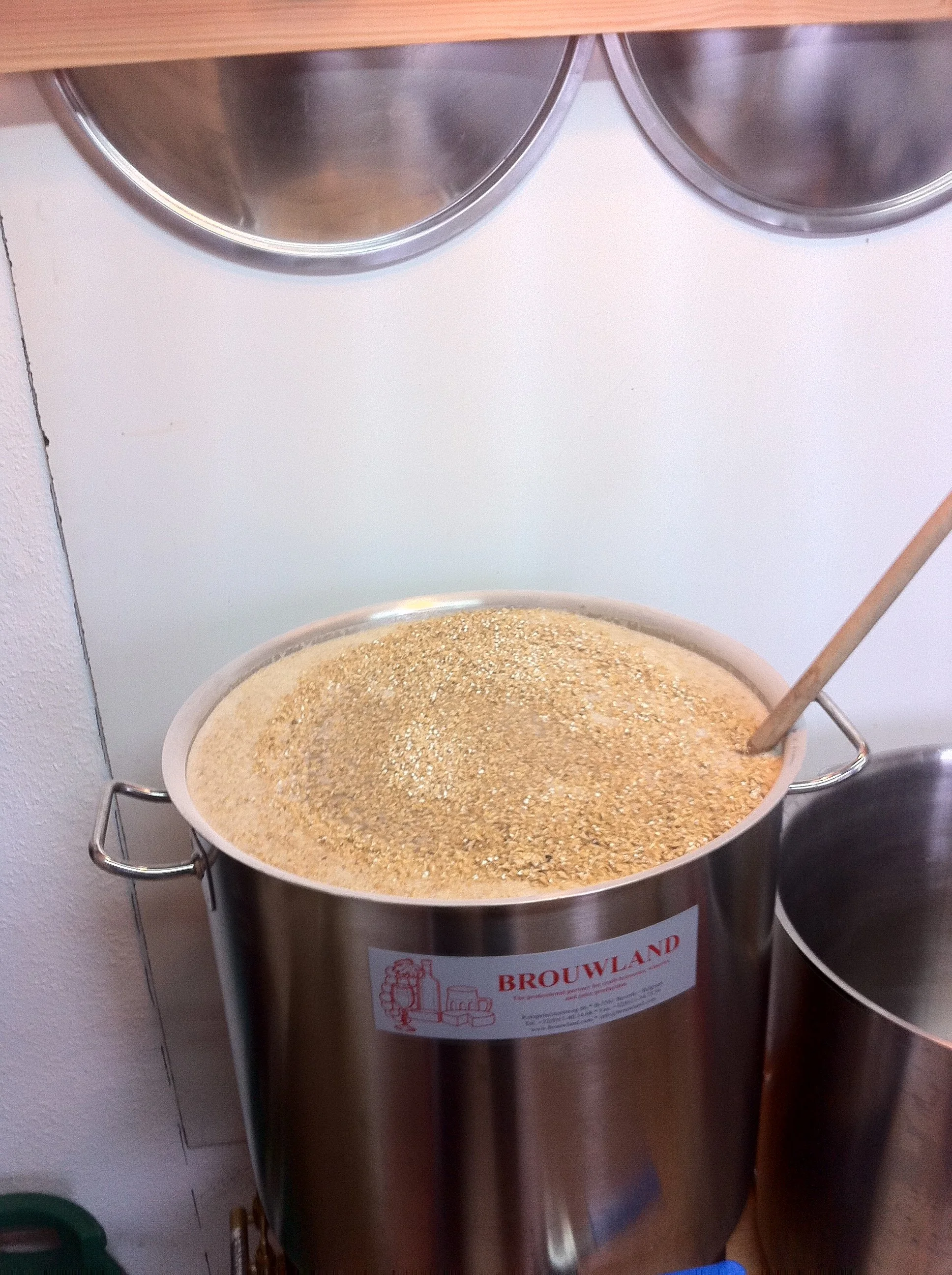 Een metalen bierkruik gevuld met gemalen granen, waarschijnlijk voor het brouwen van bier, met een lepel erin.