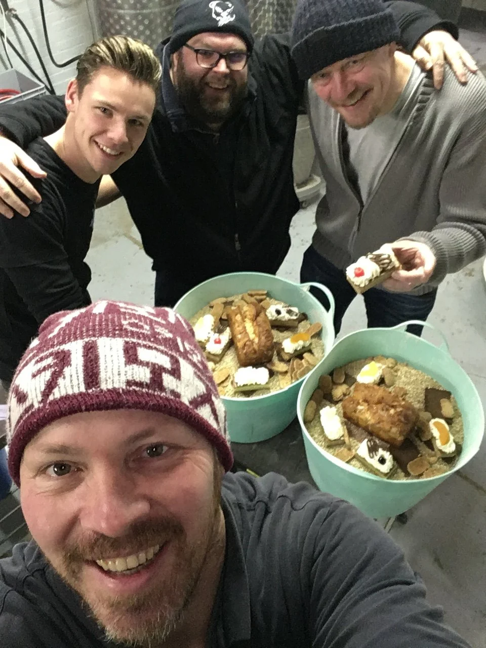 Vijf mannen die posedelen voor een foto terwijl ze bakken en eten delen, met twee bakken vol zelfgebakken zoetigheden en koekjes.