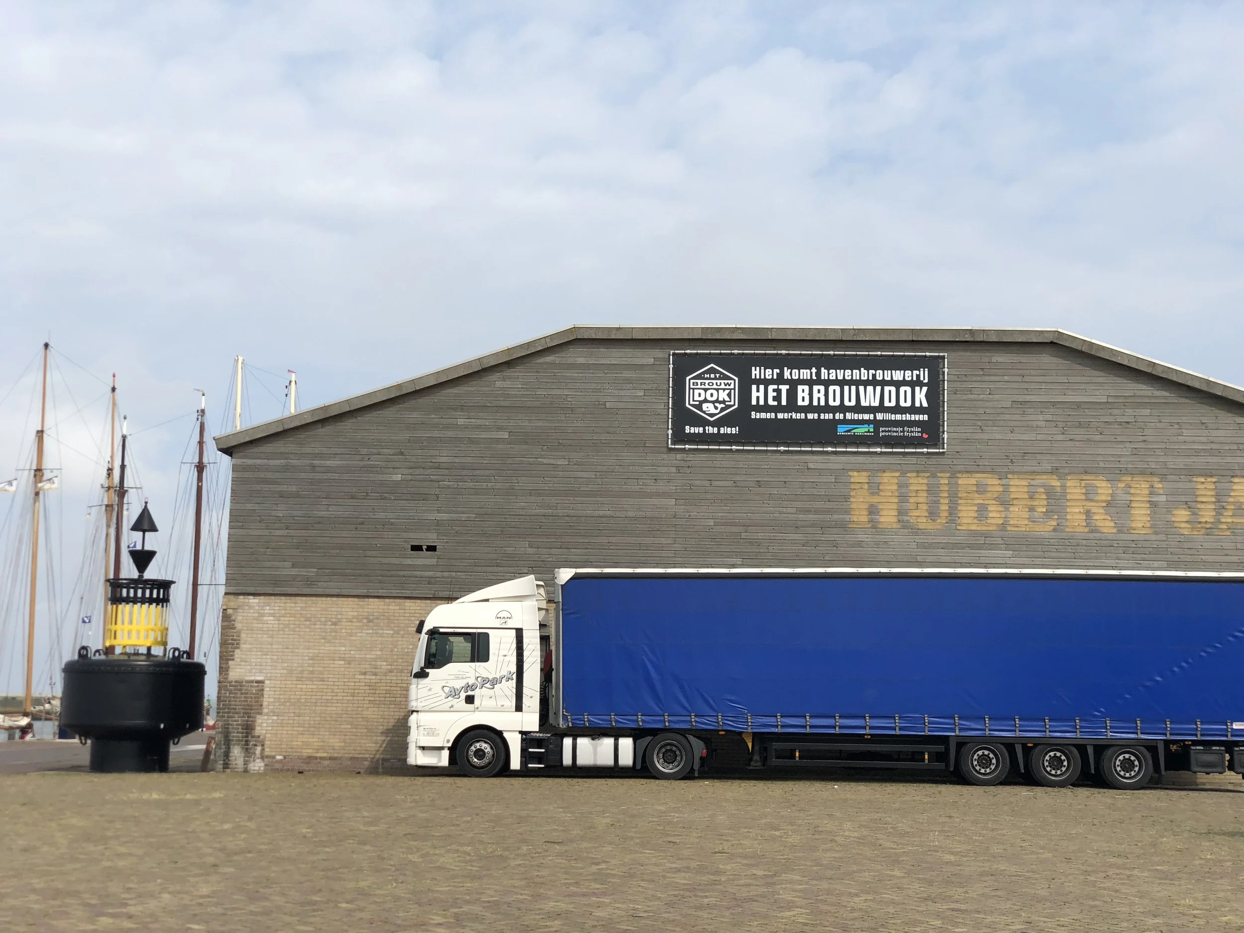 Een gebouw met een bord waarop staat dat hier de havenbrouwerij Het Brouwok komt. Er staan ook schepen en een vrachtwagen geparkeerd.