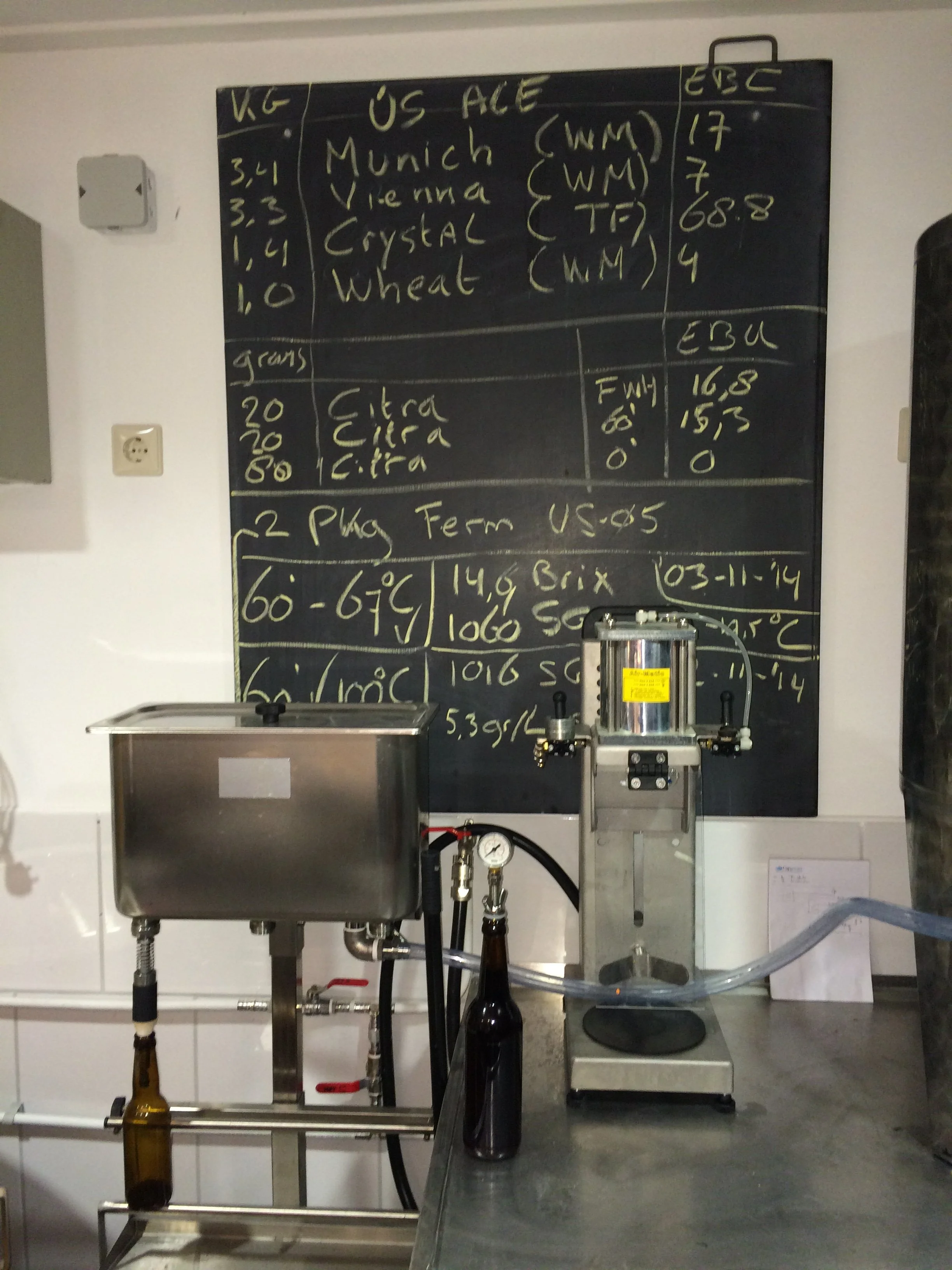 Een zwart schoolbord met daarop een lijst van biermerken en specificaties, en een proefinstallatie met flesjes en meetapparatuur op een werkbank.