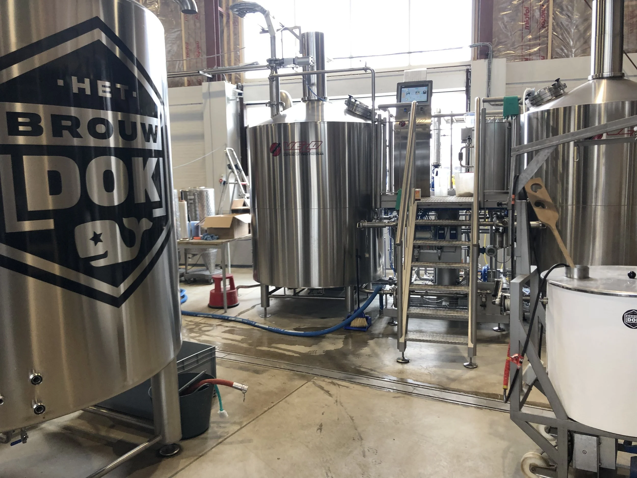 Rvs bierbrouwinstallatie in een brouwerij onder grote ramen met natuurlijke lichtinval.