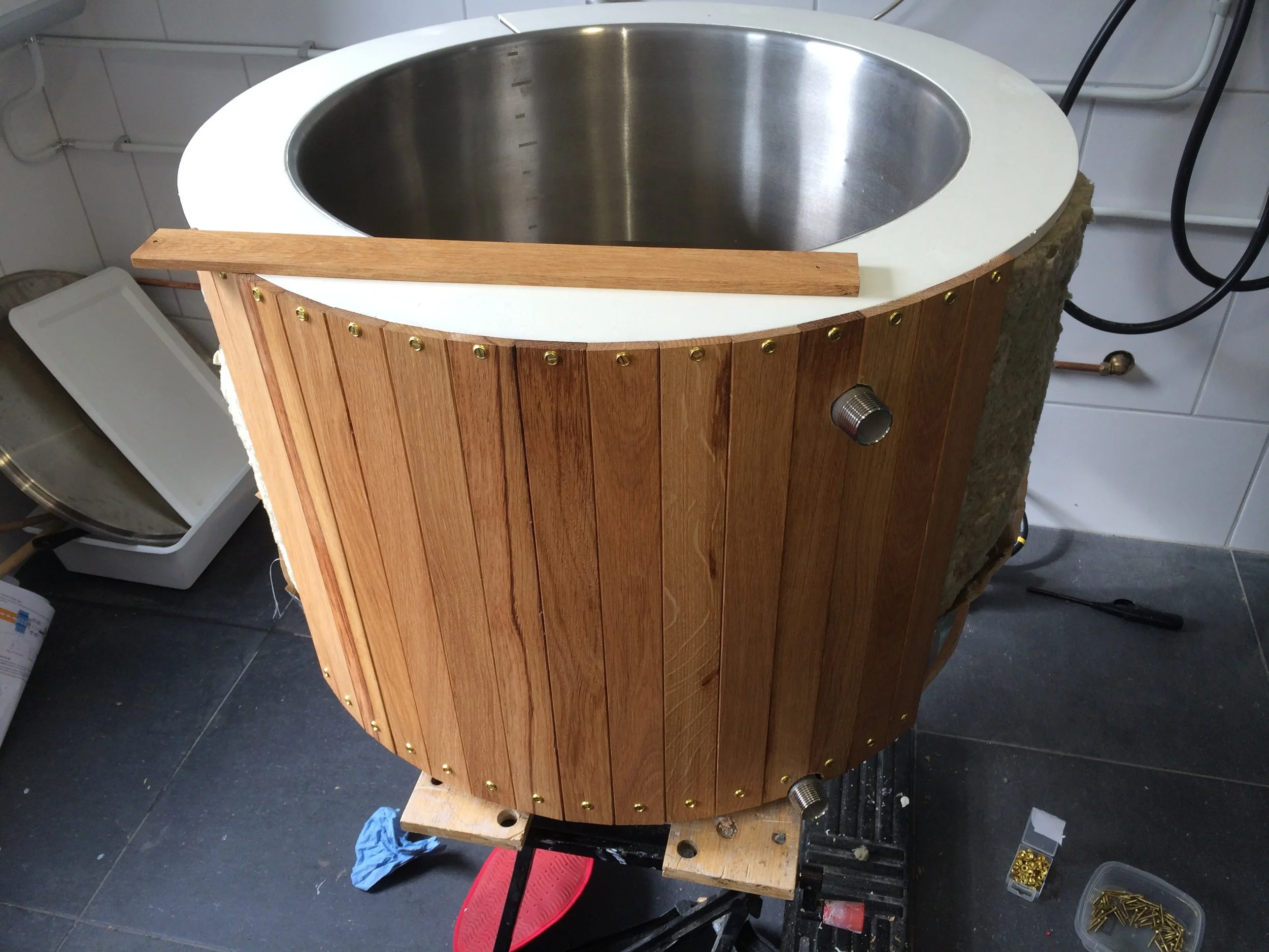 Een ronde houten constructie met een metalen rand en een afvoerpijp erin, gelegen op een werkbank in een werkplaats.
