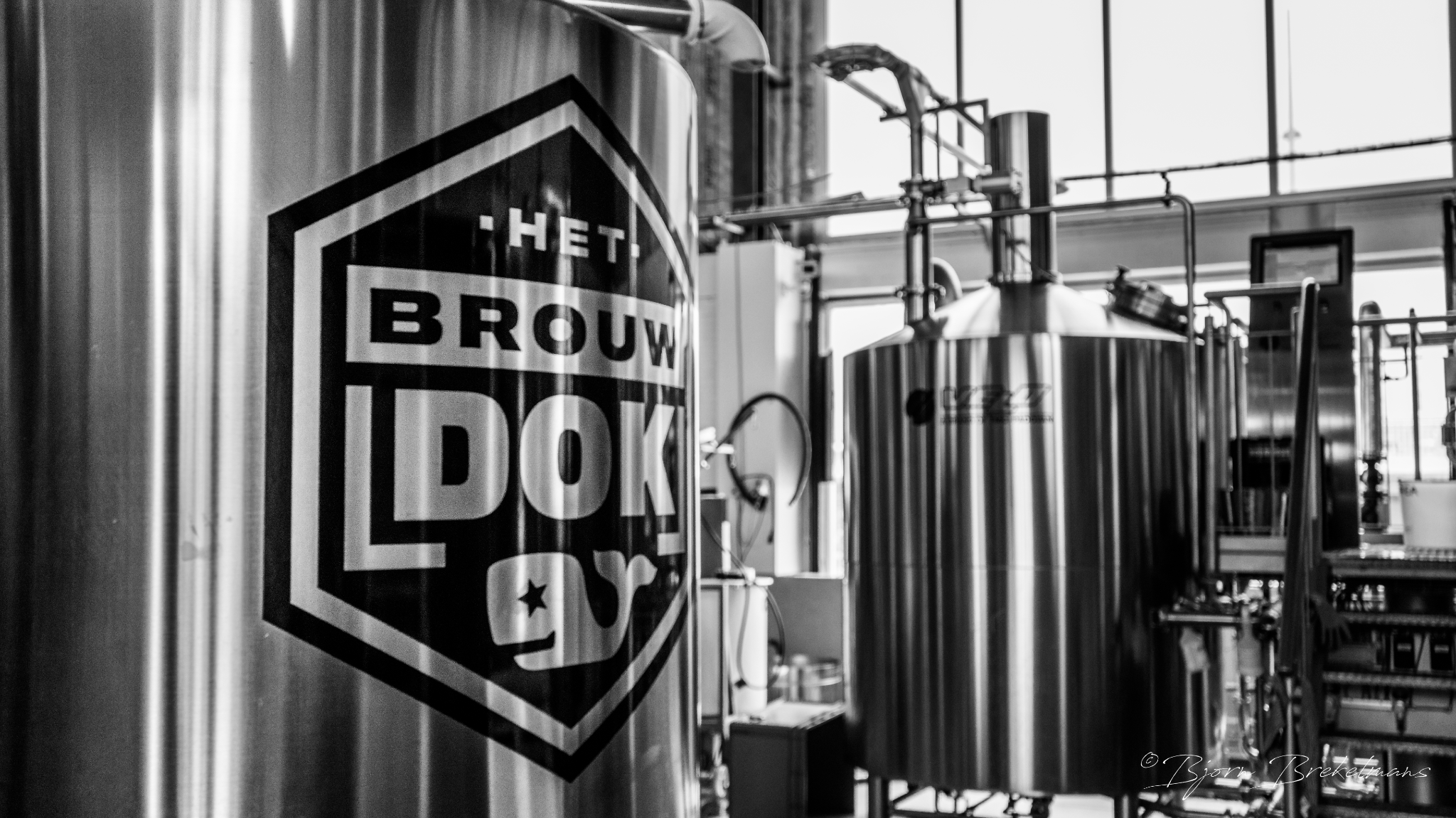 Zwarte en zilveren industriële tanks in een brouwerij met ramen die licht doorlaten.