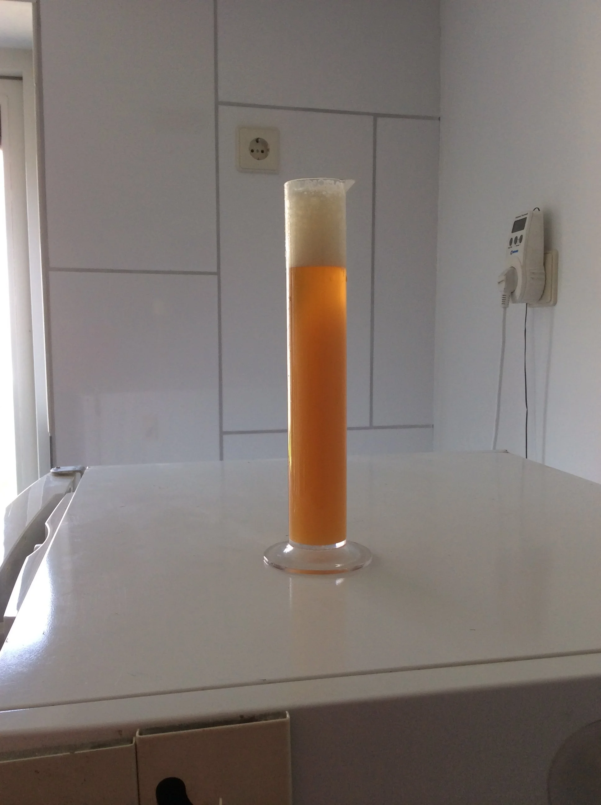 Glas met oranje en witte schuimige drank op een witte tafel in een keuken met witte tegels en een witte muur.