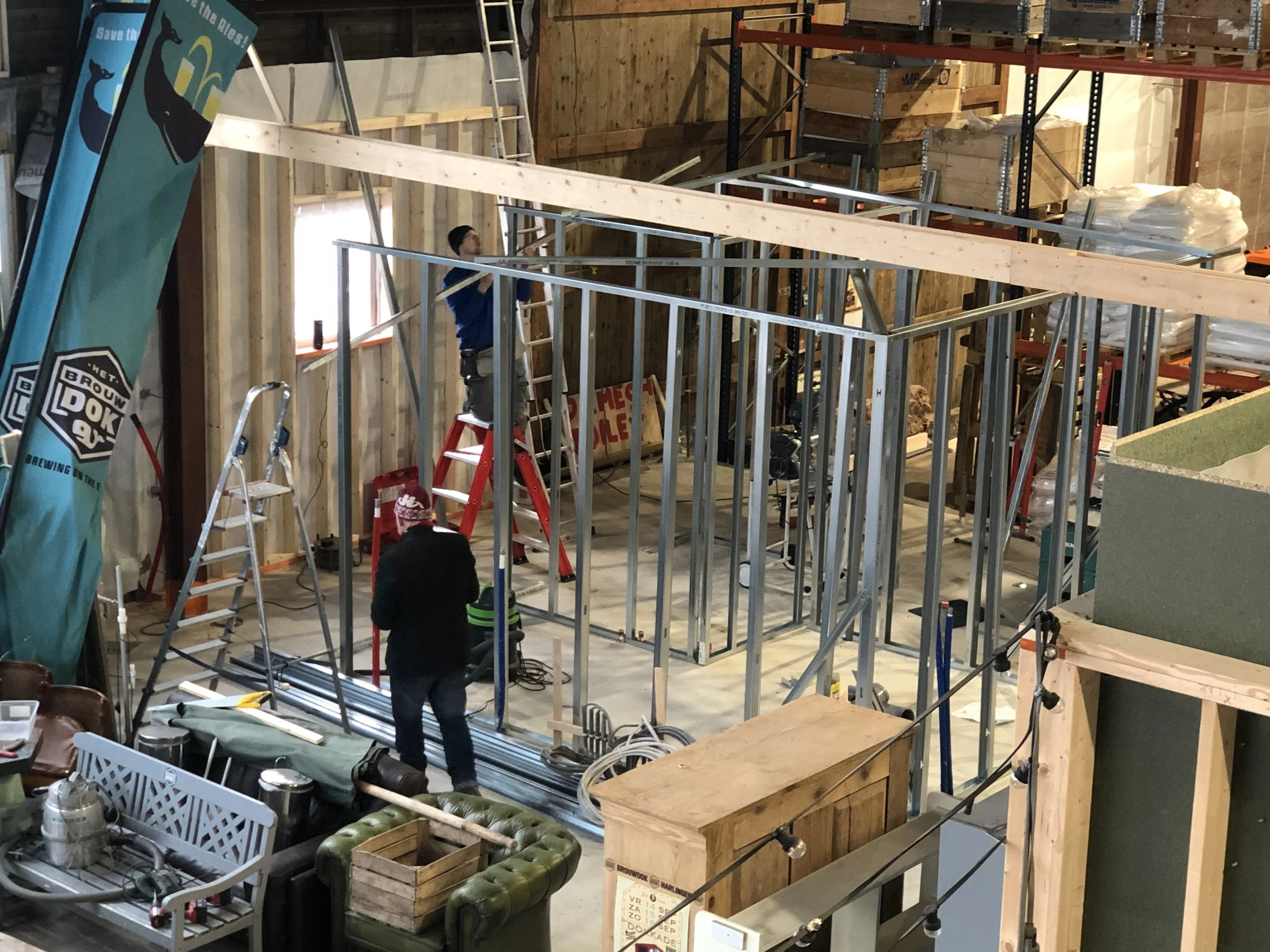 Binnen een bouwplaats met houten en metalen structuren, ladders, gereedschap en bouwmaterialen, waar mensen bezig zijn met de constructie van een frame.