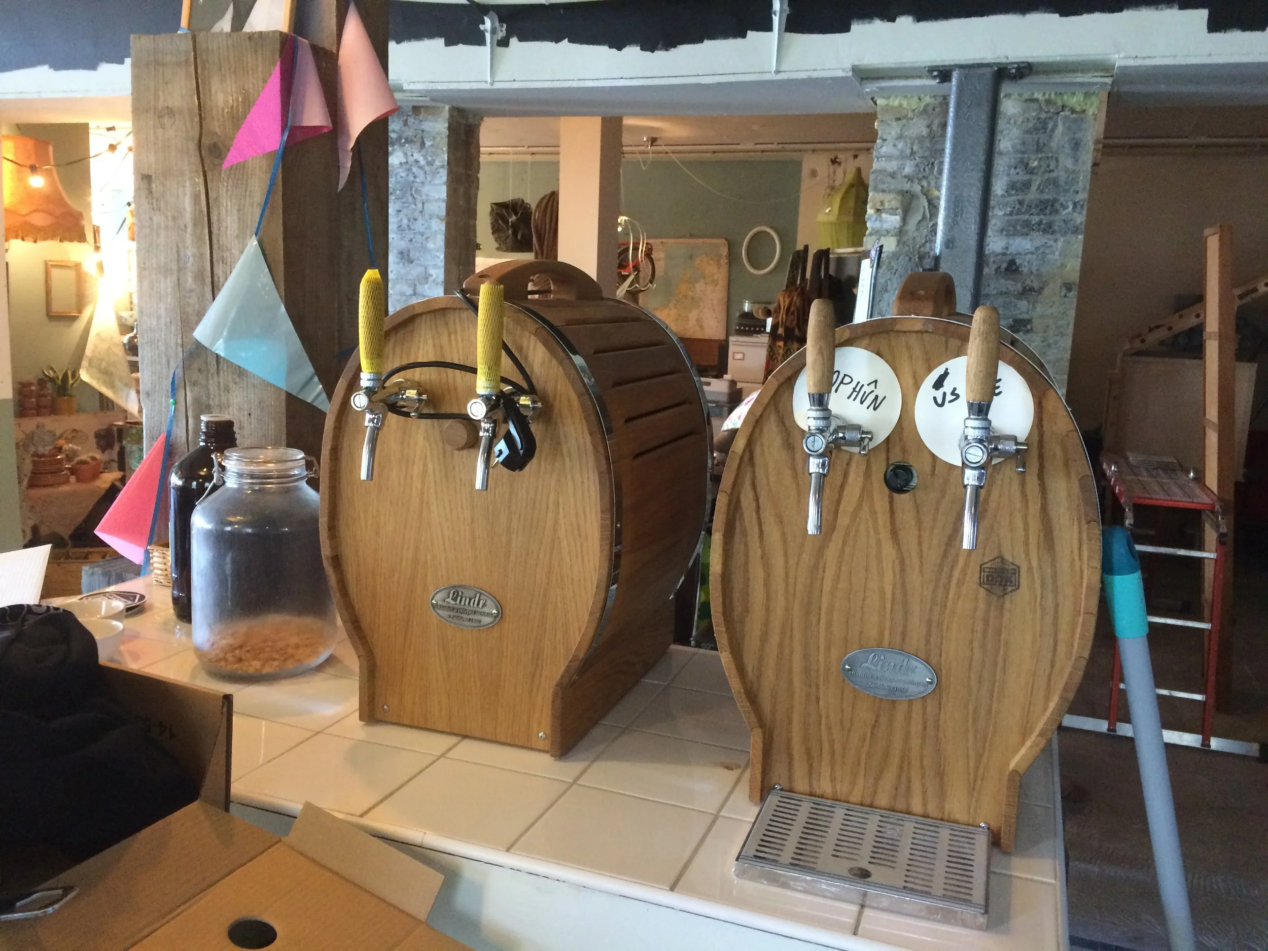 Twee houten tapkranen op een bar met een een glas met snacks en een fles water, in een restaurant of café met bakstenen muren en decoraties.