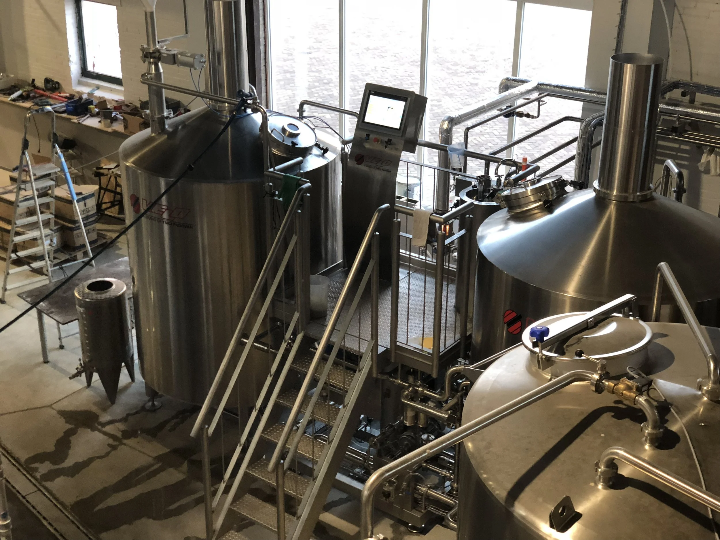 Staalvaten en technische apparatuur in een industriële ruimte, mogelijk voor brouwerijen of chemische verwerking, naast grote ramen.
