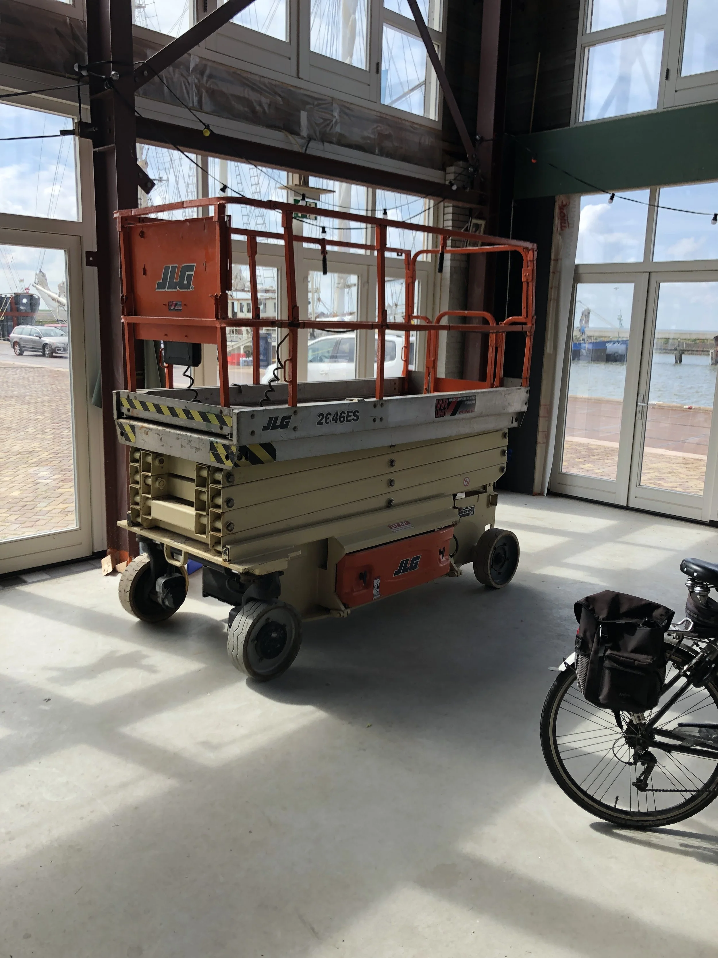 Een binnenruimte met grote ramen, een hoogtewerker en een fiets.