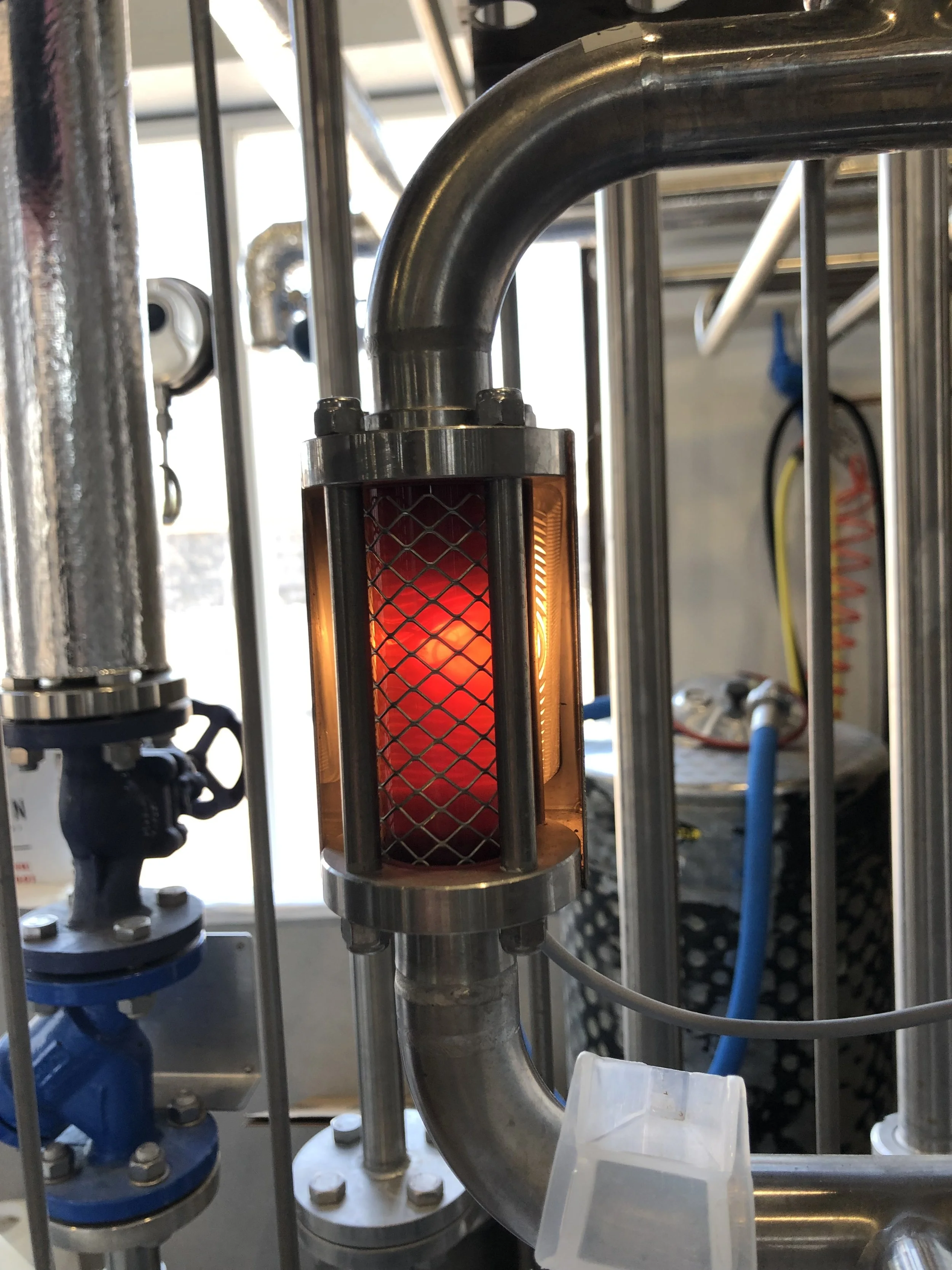 Een close-up van een labapparaat met een glanzende metalen buis en een verwarmingsbad dat rood gloeit, omgeven door een metalen rooster en voorzien van verschillende andere laboratoriuminstrumenten en buizen.