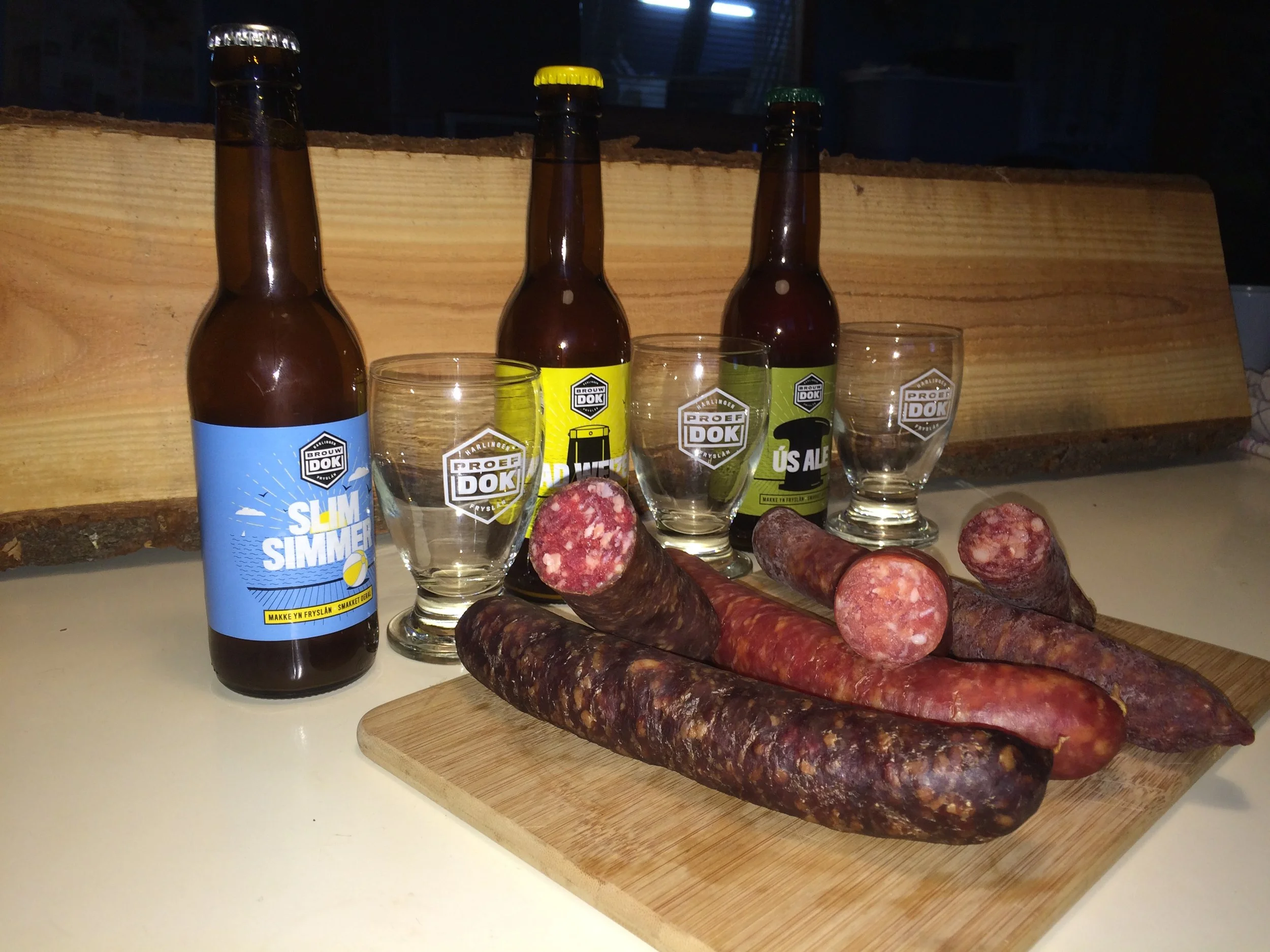 Verschillende geurige worsten en bierflesjes op een snijplank, met een houten achtergrond