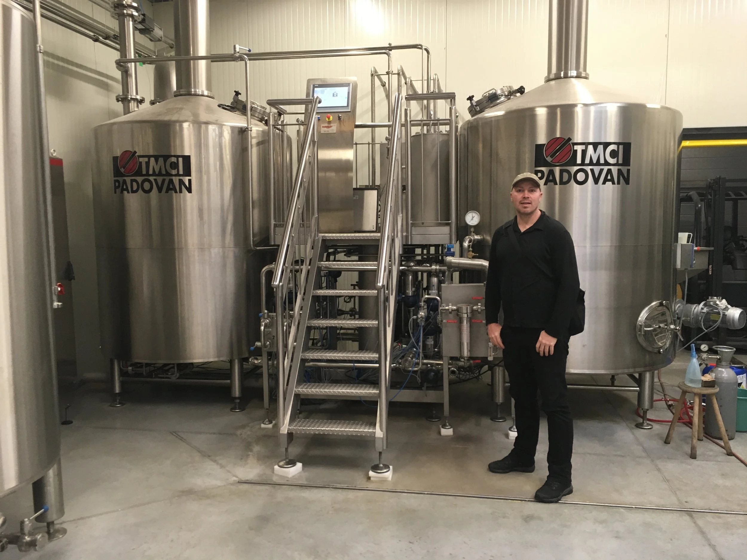 Een man die in een industrieel lab of brouwerij ruimte staat voor grote metalen biertank met het logo 'TMCI Padovan'.