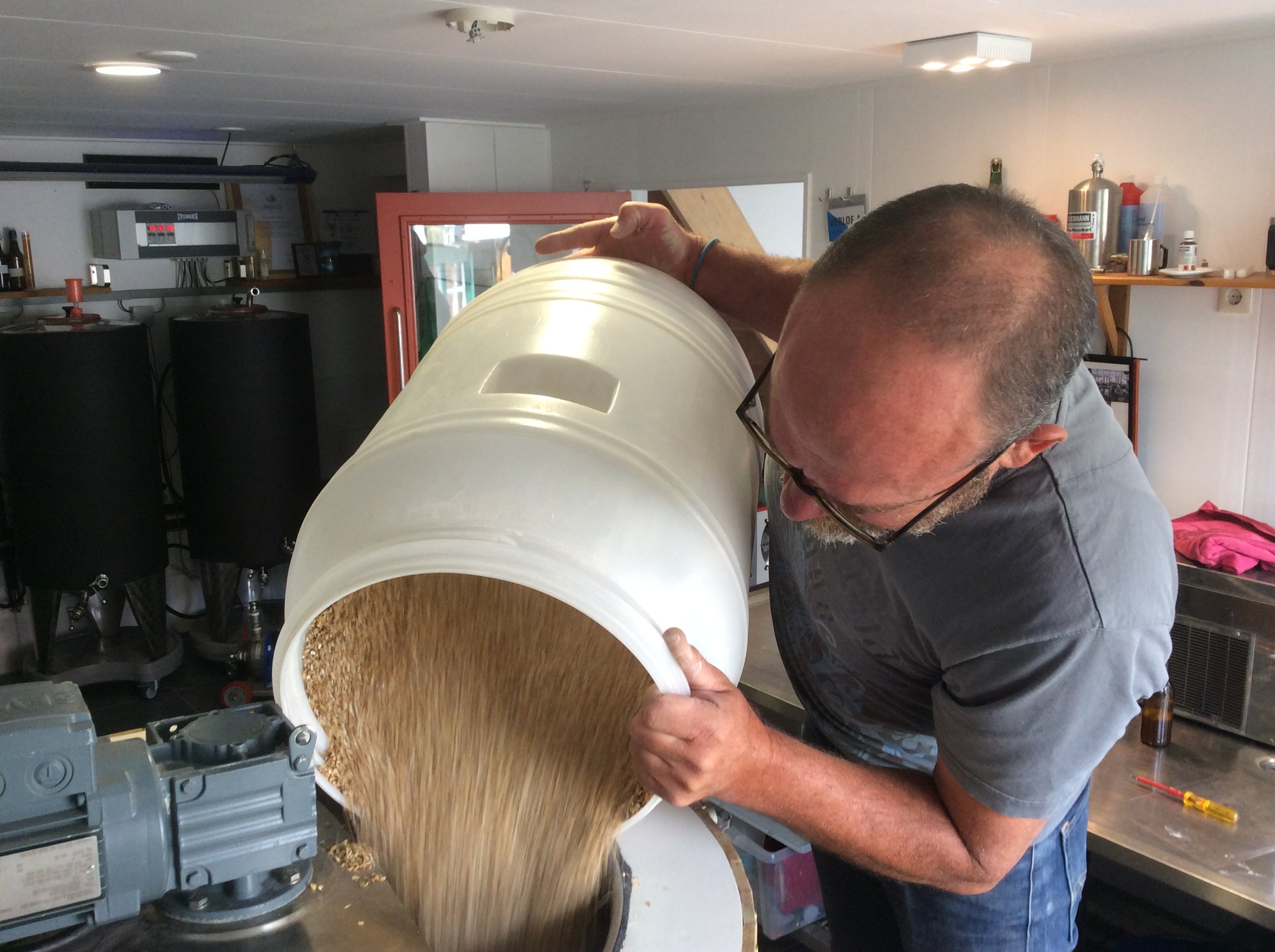Man giet graan uit een grote witte ton in een machine.