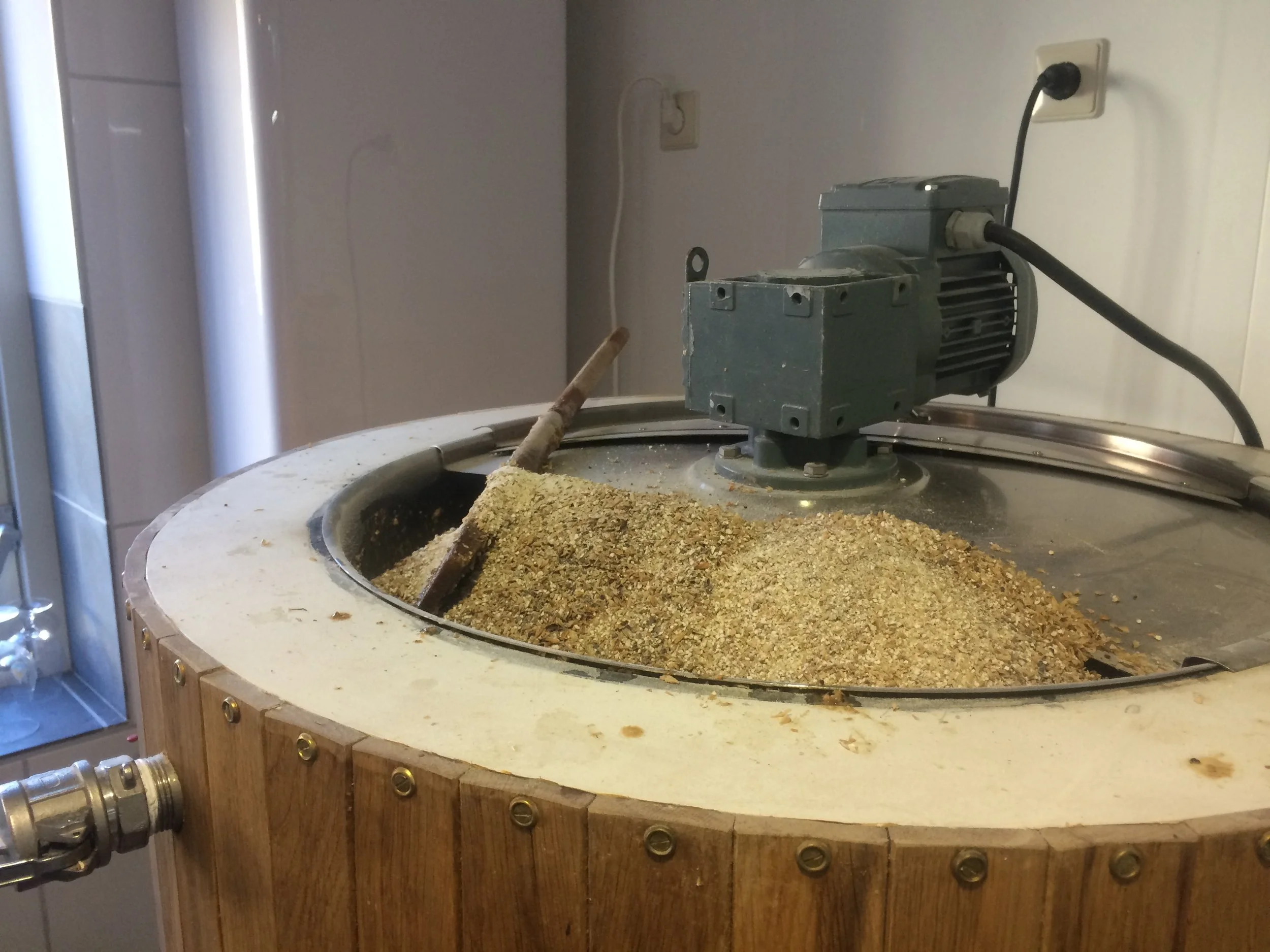 een industriële tafel met een draaiende motor en een houten rand, gevuld met een mengsel van granen en plantenmateriaal.