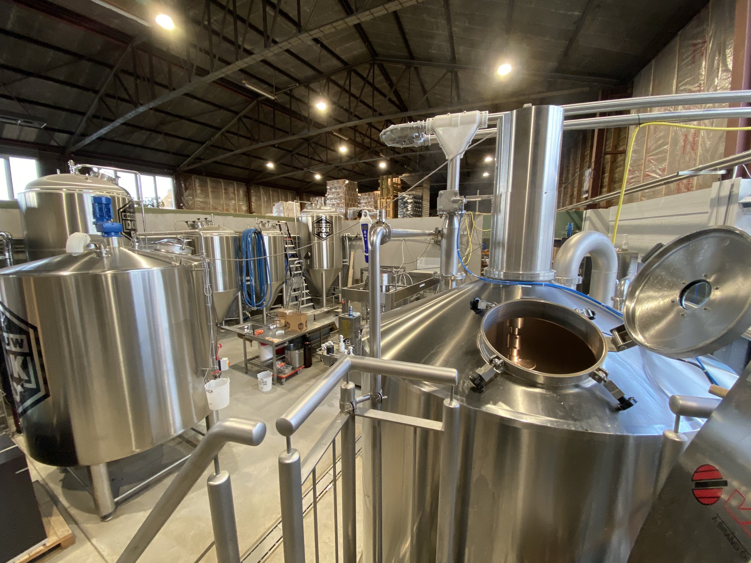 Binnenin een industriële ruimte met grote stalen tanks en piping, waarschijnlijk een brouwerij of chemisch productiegebouw.