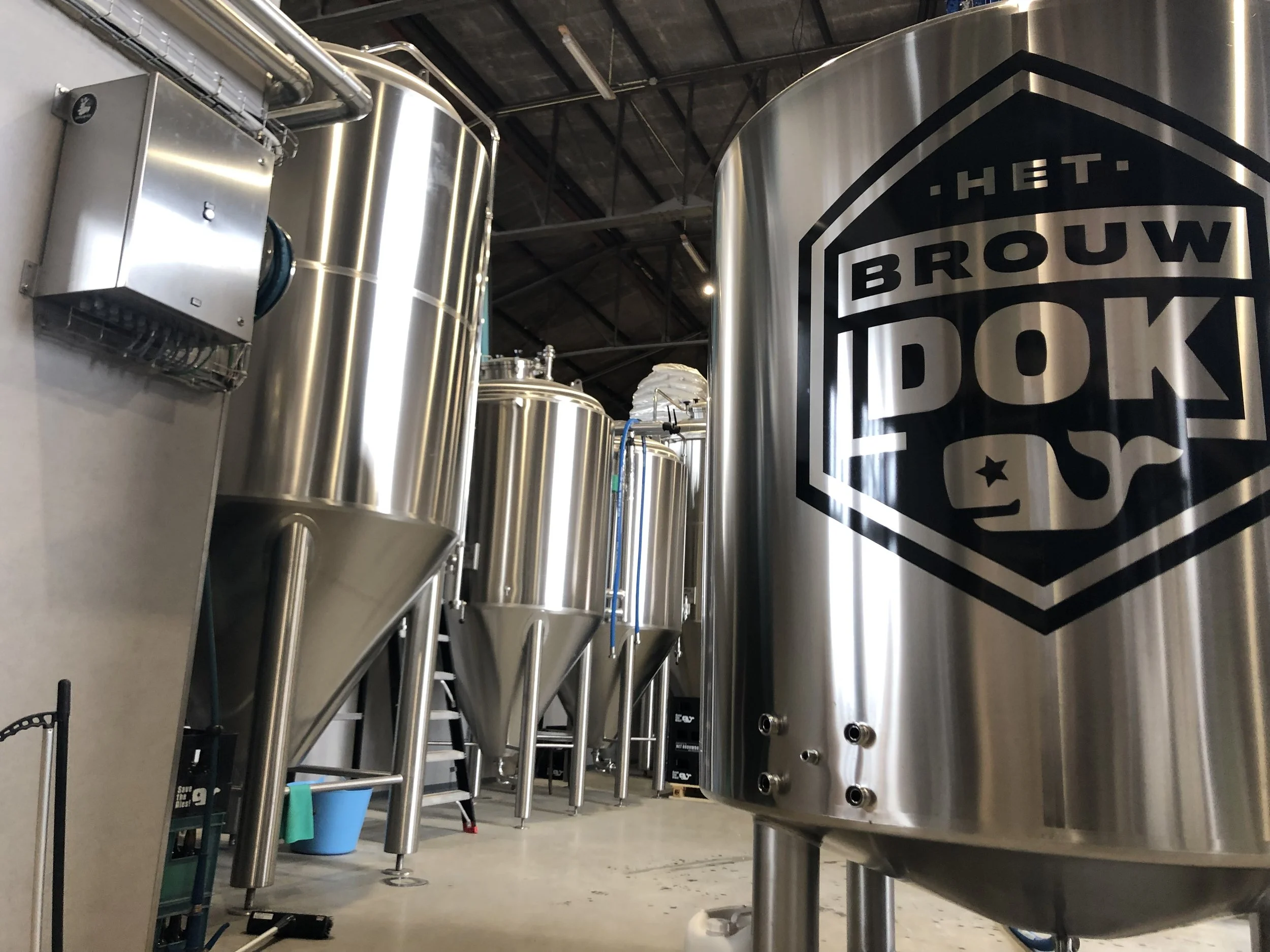 Rvs tanks en apparatuur in een brouwerij, met een groot logo van 'HET BROUWKLOED' op een tank.