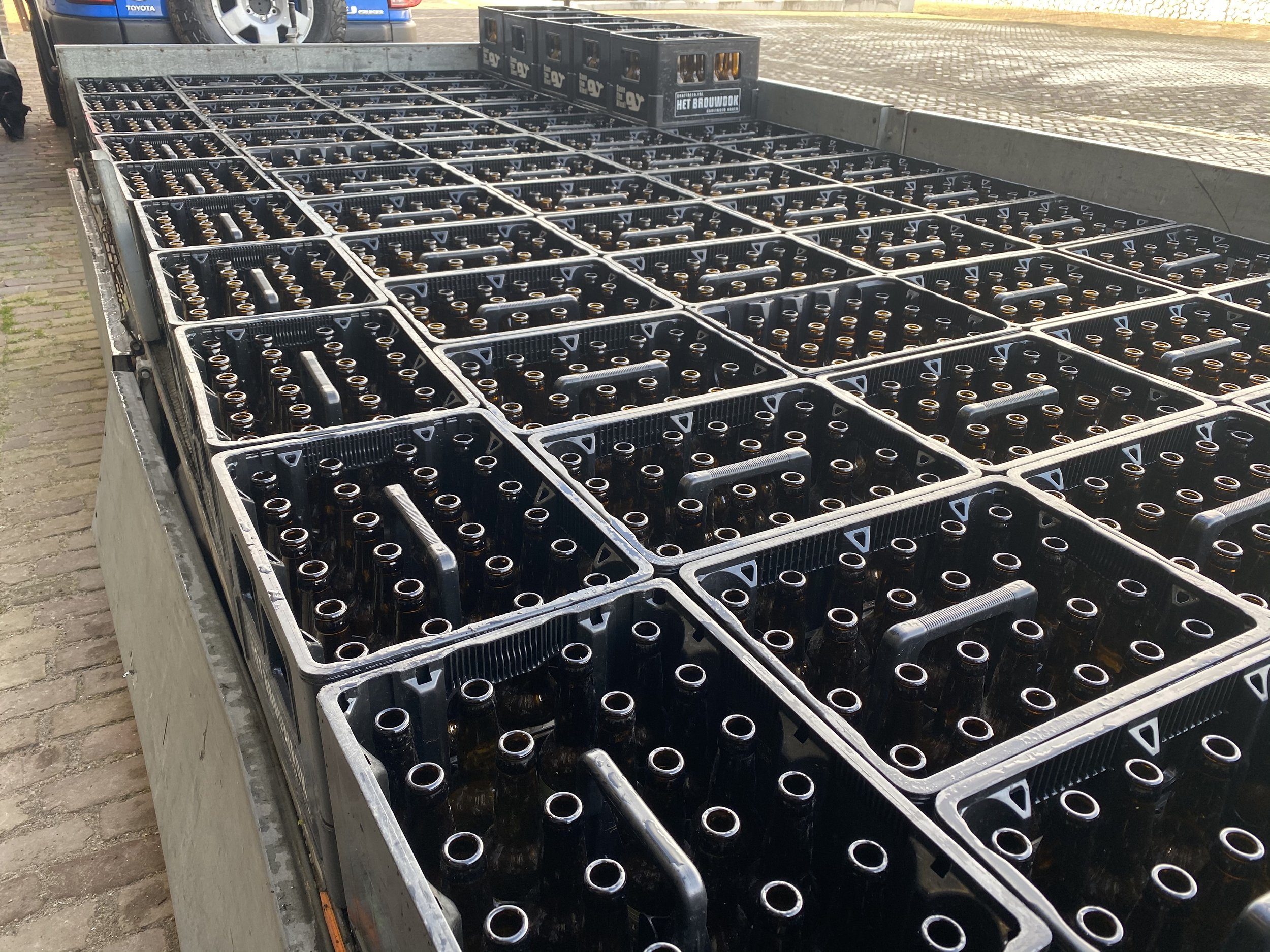 Boten met lege glazen bierflessen op een laadbak buiten, nabij een parkeergarage.