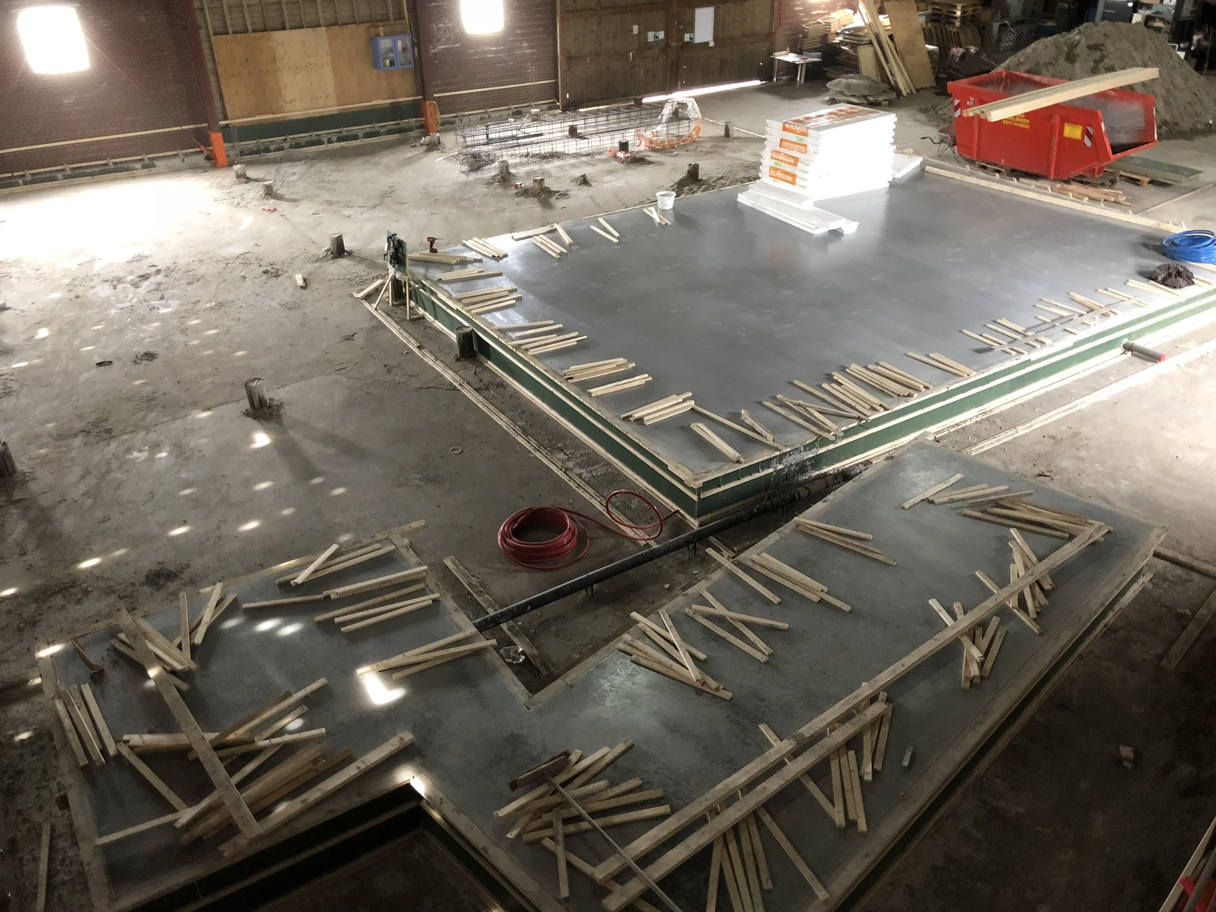 Binnen in een bouwplaats met betonnen vloer, hout en bouwmaterialen zoals verf en isolatie, klaar voor verdere constructie.