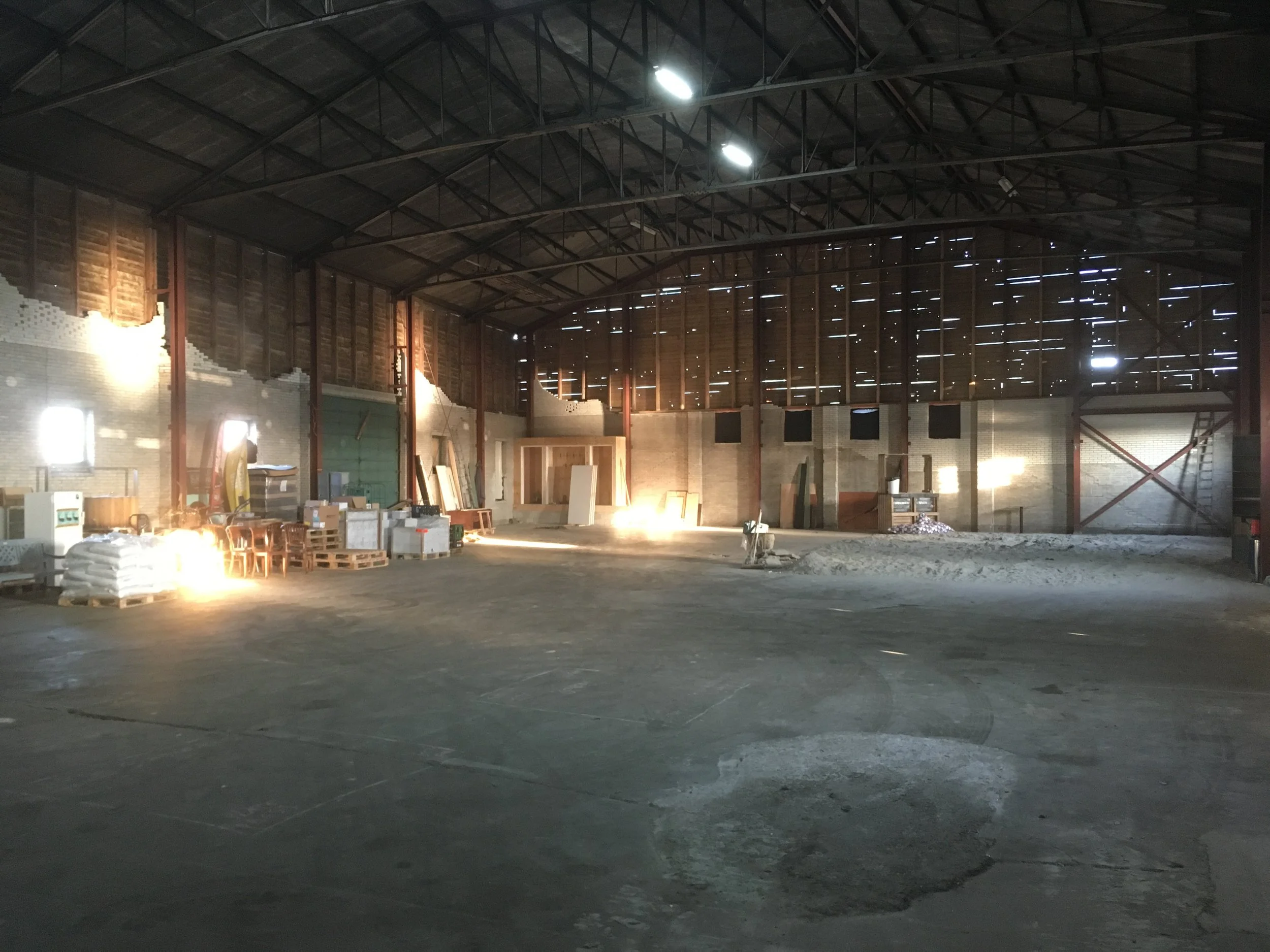 Interieur van een gebouw dat nog in aanbouw is, met grote open ruimte, houten en metalen structuur, en bouwmaterialen en gereedschap op de vloer.