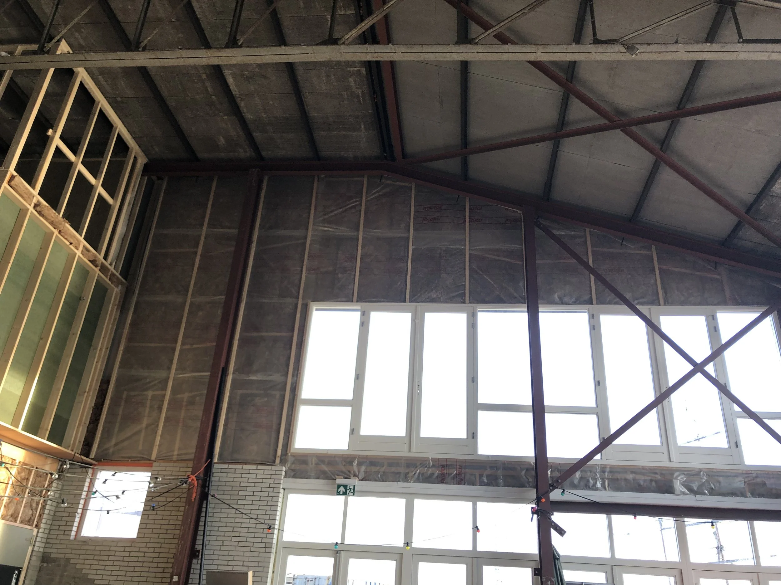 Binnenkant van een gebouw in aanbouw met zichtbaar metaalbouw, hout en ramen onder een hoog plafond.